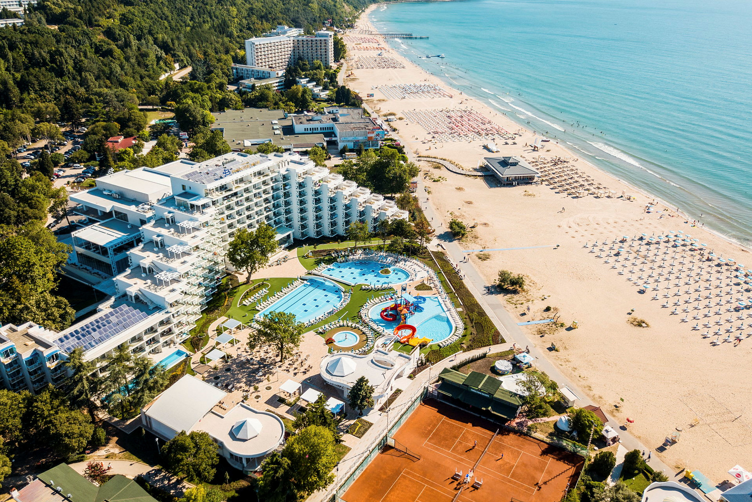 Ilmakuva hotellista, jossa on allasalue, viheralueita ja ranta. (Tekoälyn luoma teksti)