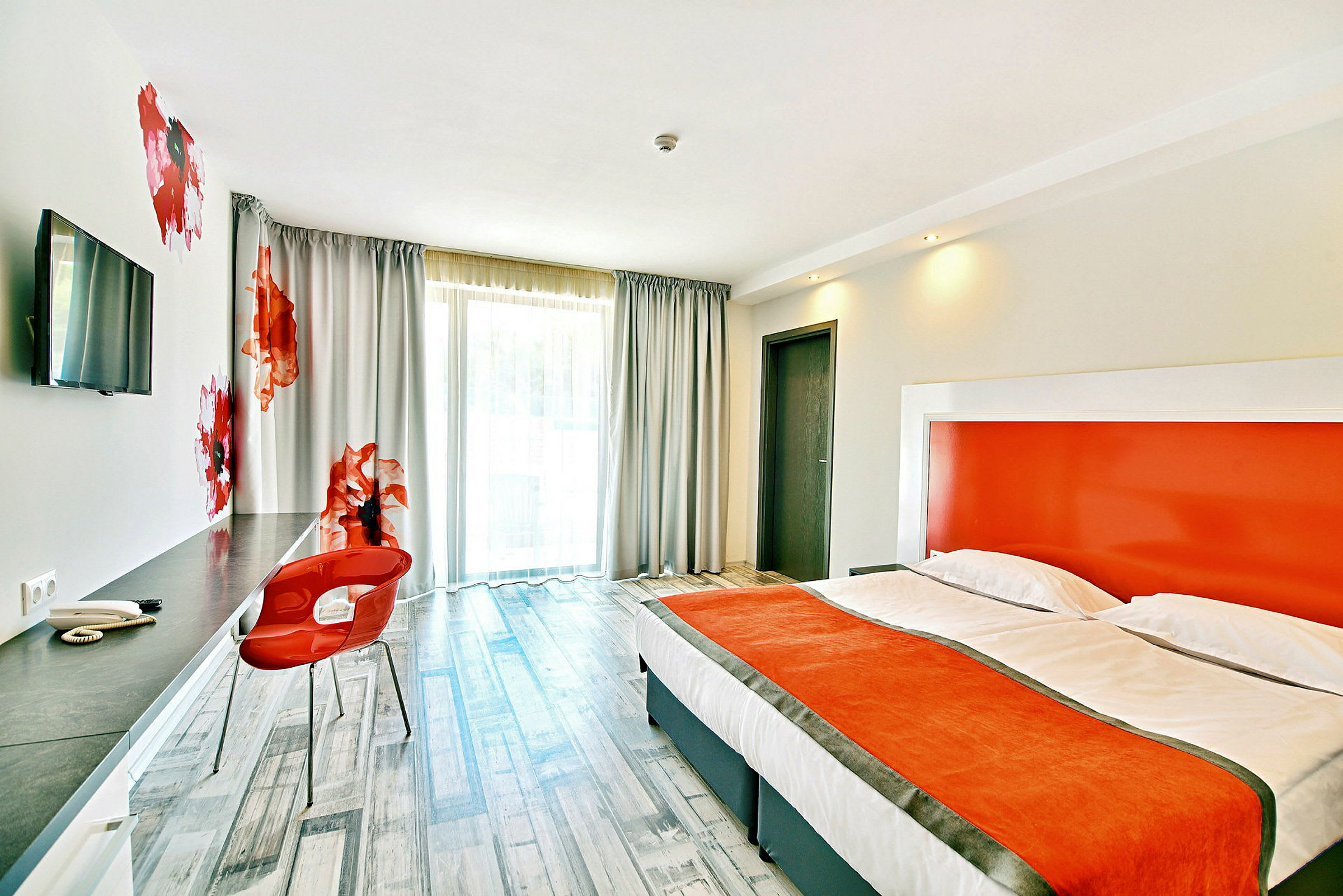 Moderni hotellihuone, jossa oransseja yksityiskohtia, mukava sänky ja työalue. (Tekoälyn luoma teksti)