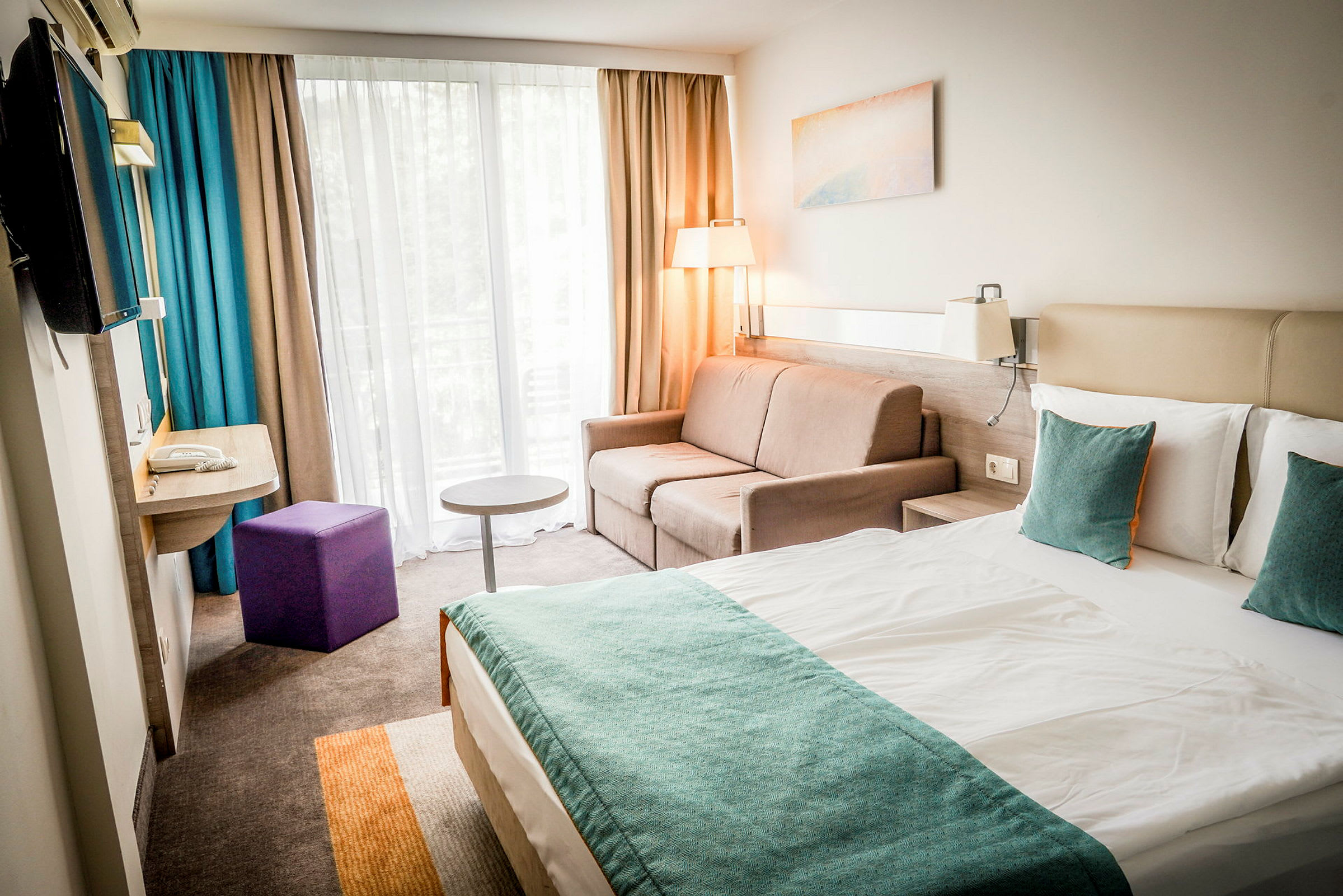 Nykyaikainen hotellihuone, jossa on parivuode, sohva ja ikkuna verhoineen. (Tekoälyn luoma teksti)