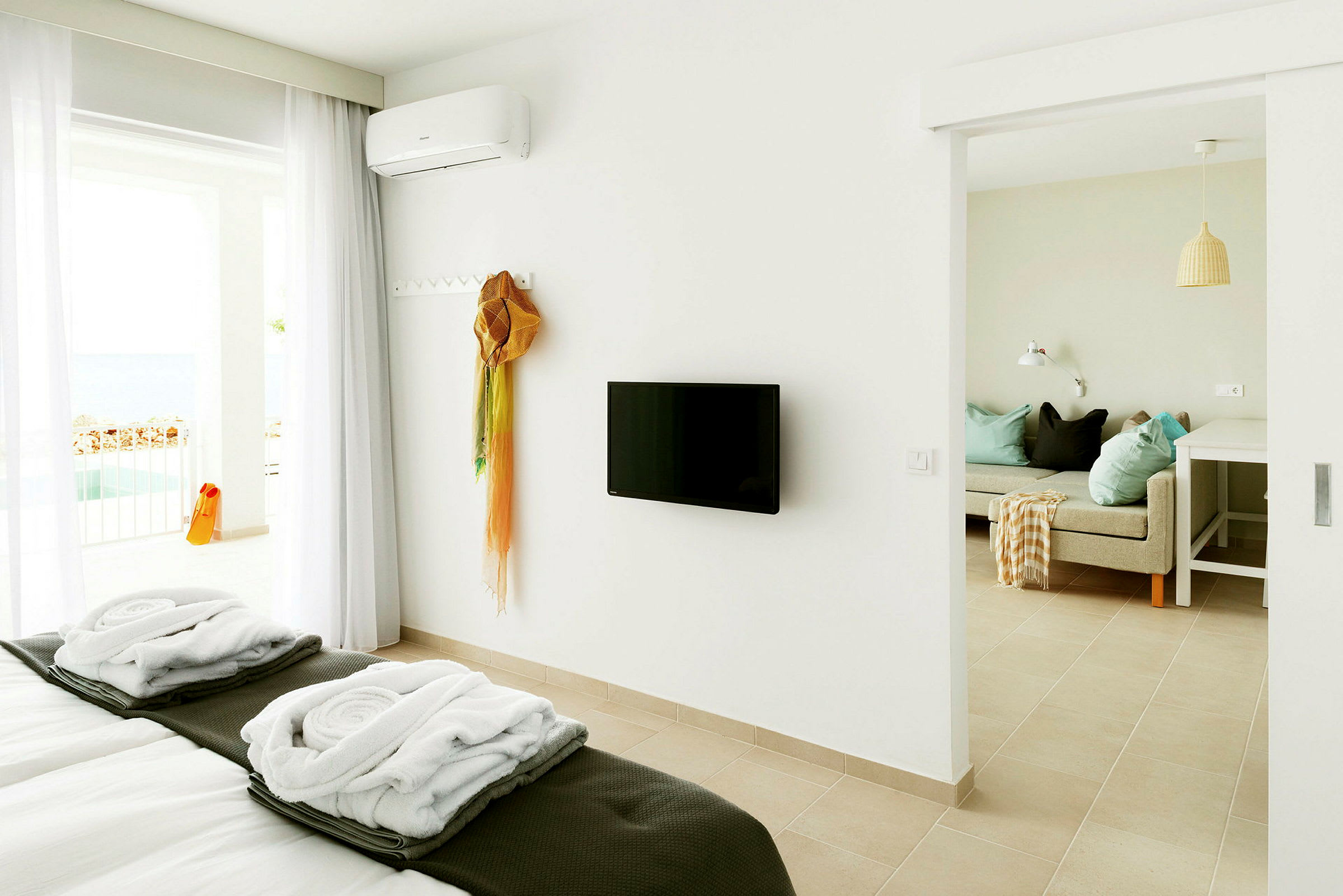 Valoisa hotellihuone, jossa pedattu sänky, seinään asennettu TV ja istuinalue. Taustalla näkyy parveke näkymällä. (Tekoälyn luoma teksti)