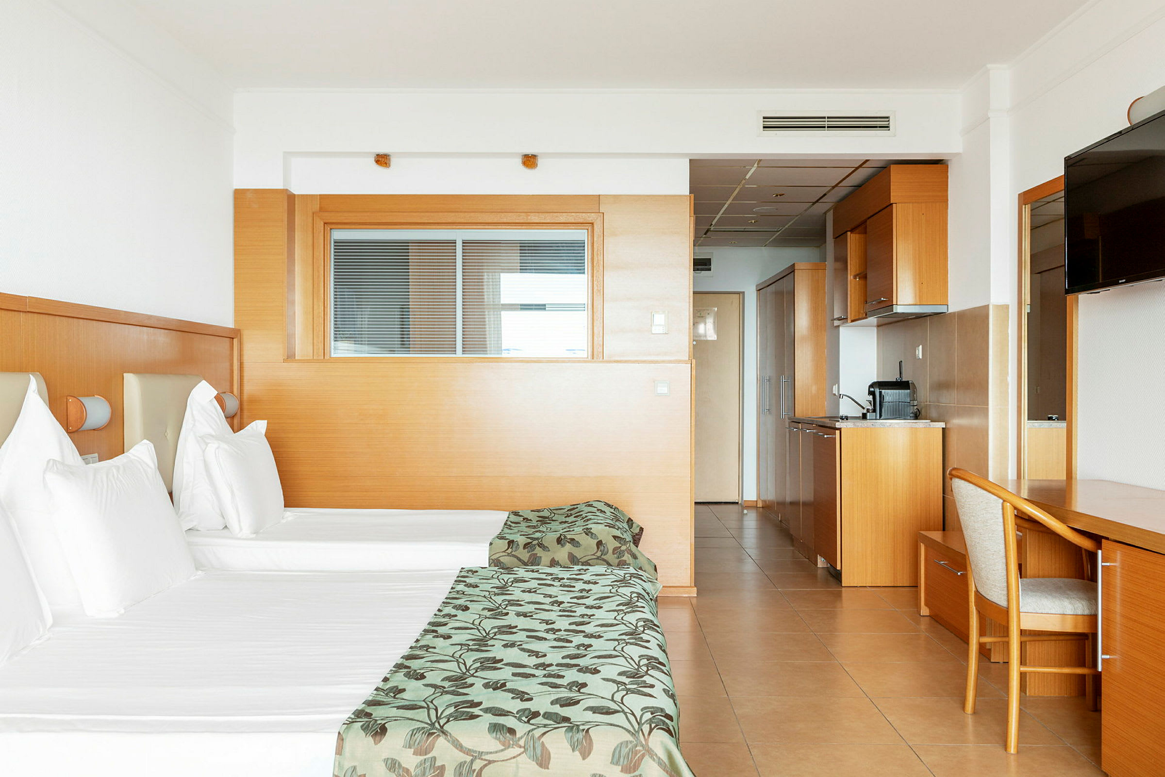 Hotellihuone kahdella erillisellä vuoteella, keittiöosa ja kirjoituspöytä. (Tekoälyn luoma teksti)