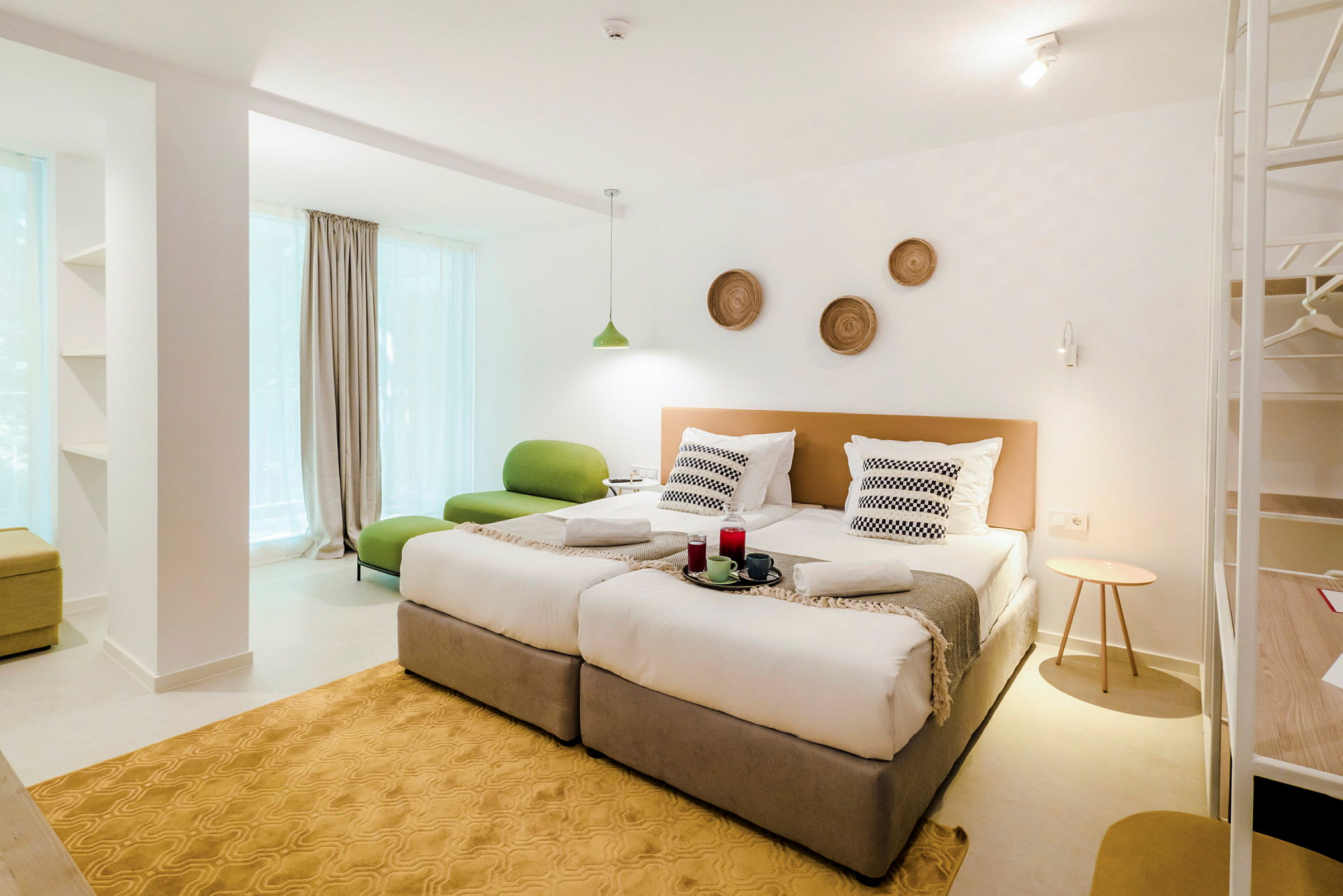 Moderni hotellihuone, jossa kaksi erillistä vuodetta, vihreä istuin ja koristeita seinällä. (Tekoälyn luoma teksti)