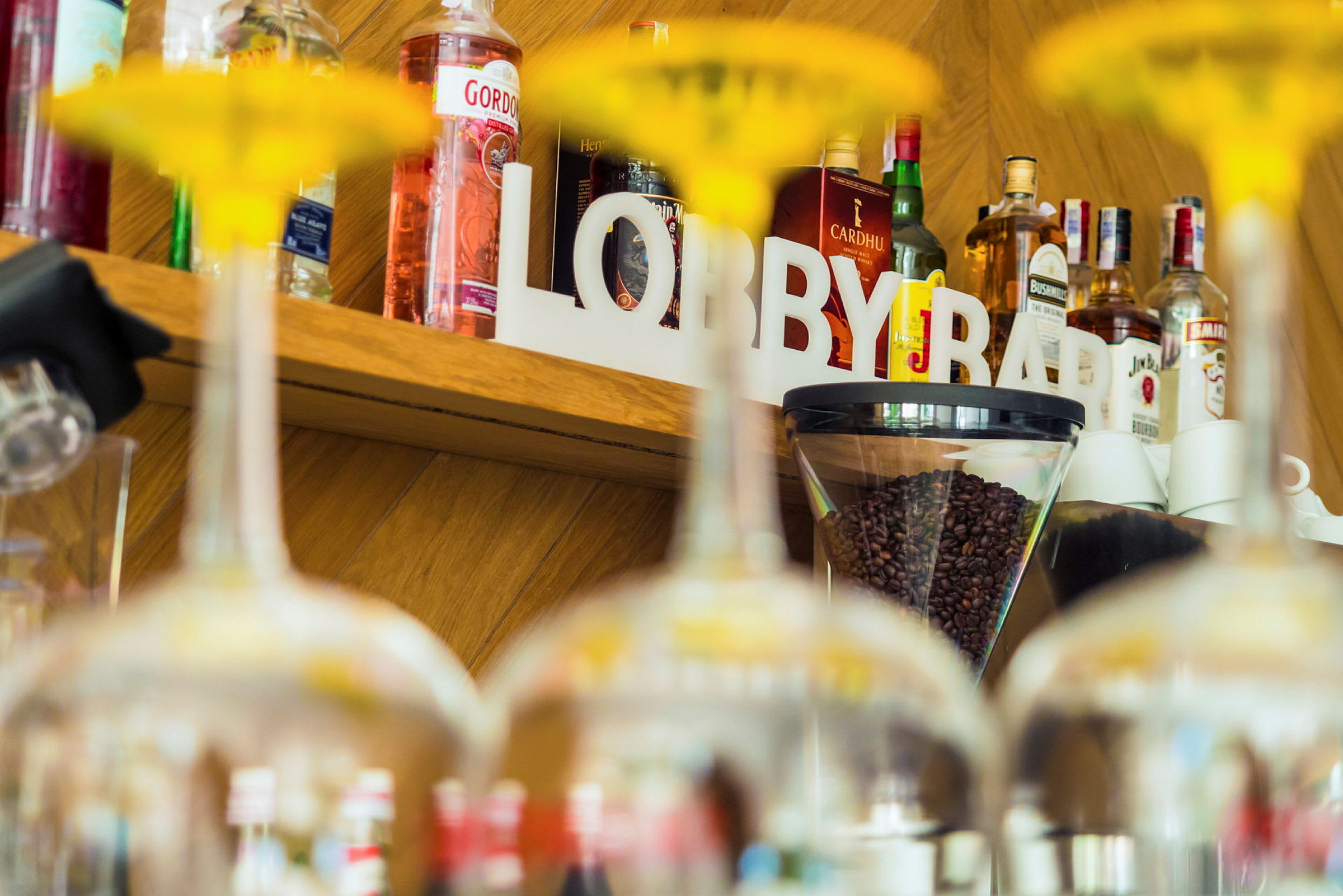 Hyllyllä on pulloja, kahvipapuja ja teksti 'LOBBY BAR', jotka näkyvät lasien takaa. (Tekoälyn luoma teksti)