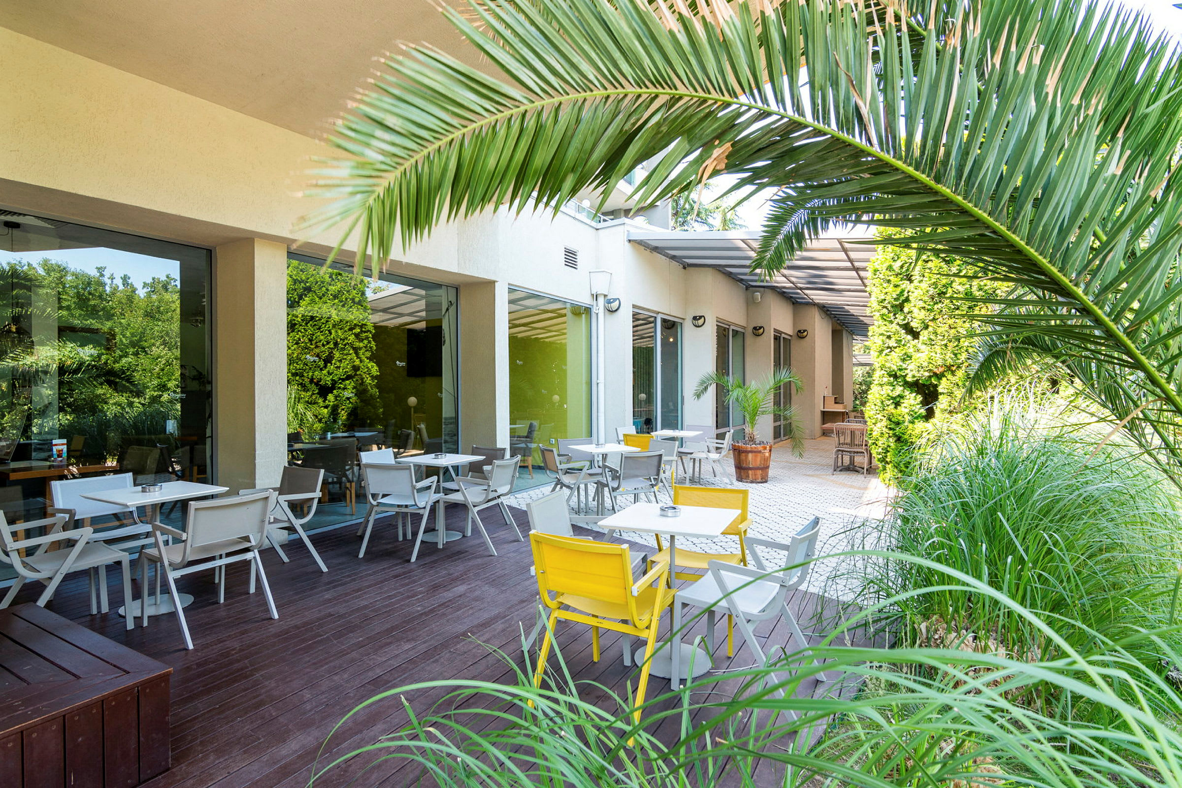Ulkoalue, jossa on pöytiä ja tuoleja, ympäröitynä vihreillä kasveilla. (Tekoälyn luoma teksti)