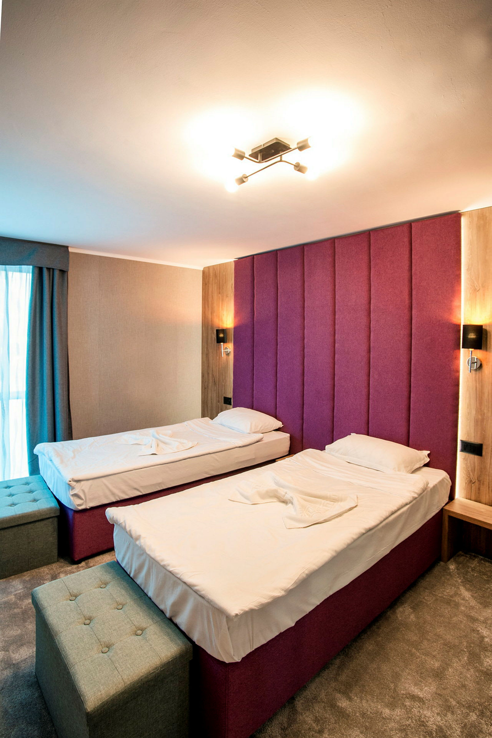 Hotellihuone, jossa on kaksi yhden hengen sänkyä, lila pääty ja moderni sisustus. (Tekoälyn luoma teksti)