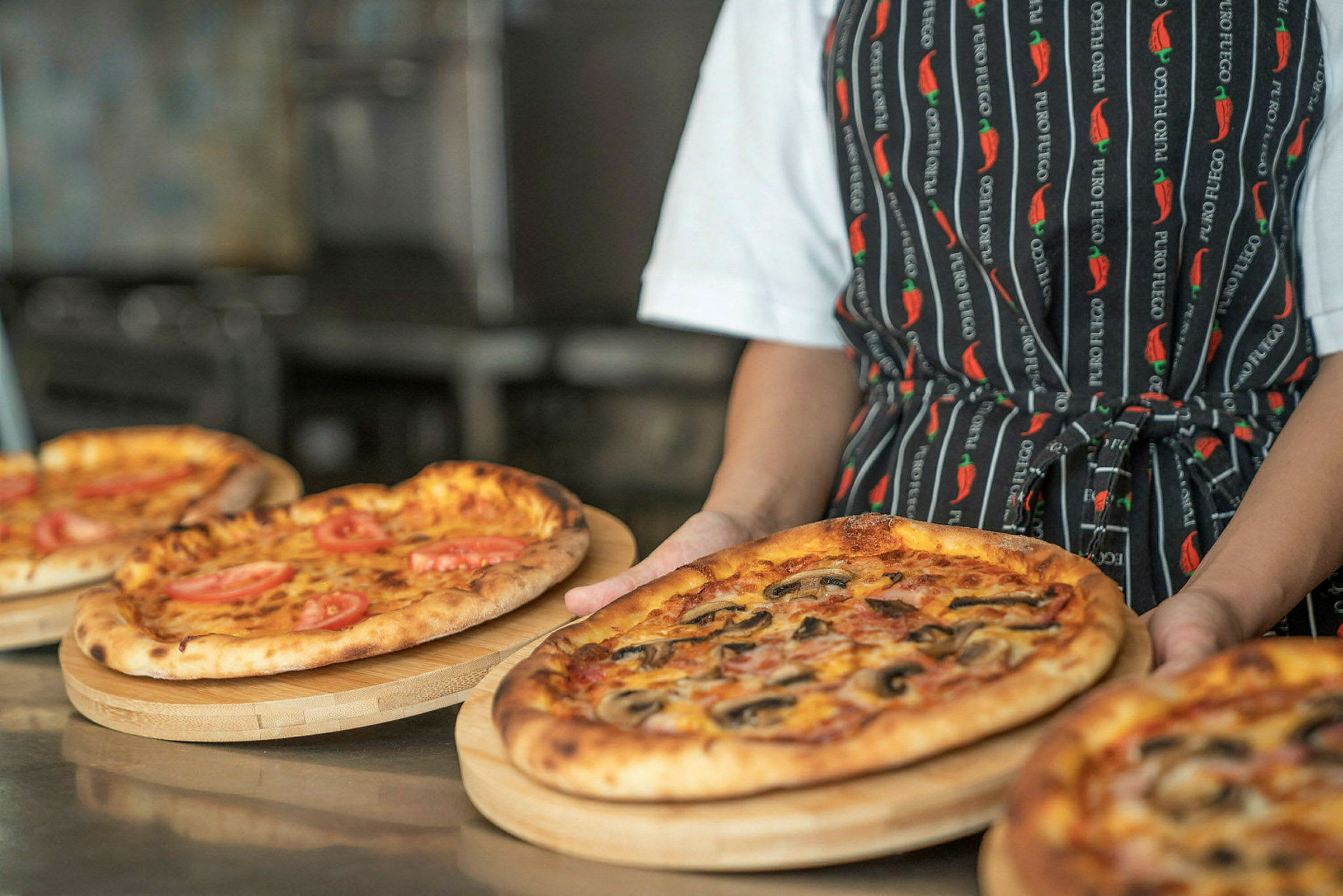 Henkilö pitää puutarjotinta, jossa on pizza, ympäröitynä muilla pizzoilla. (Tekoälyn luoma teksti)