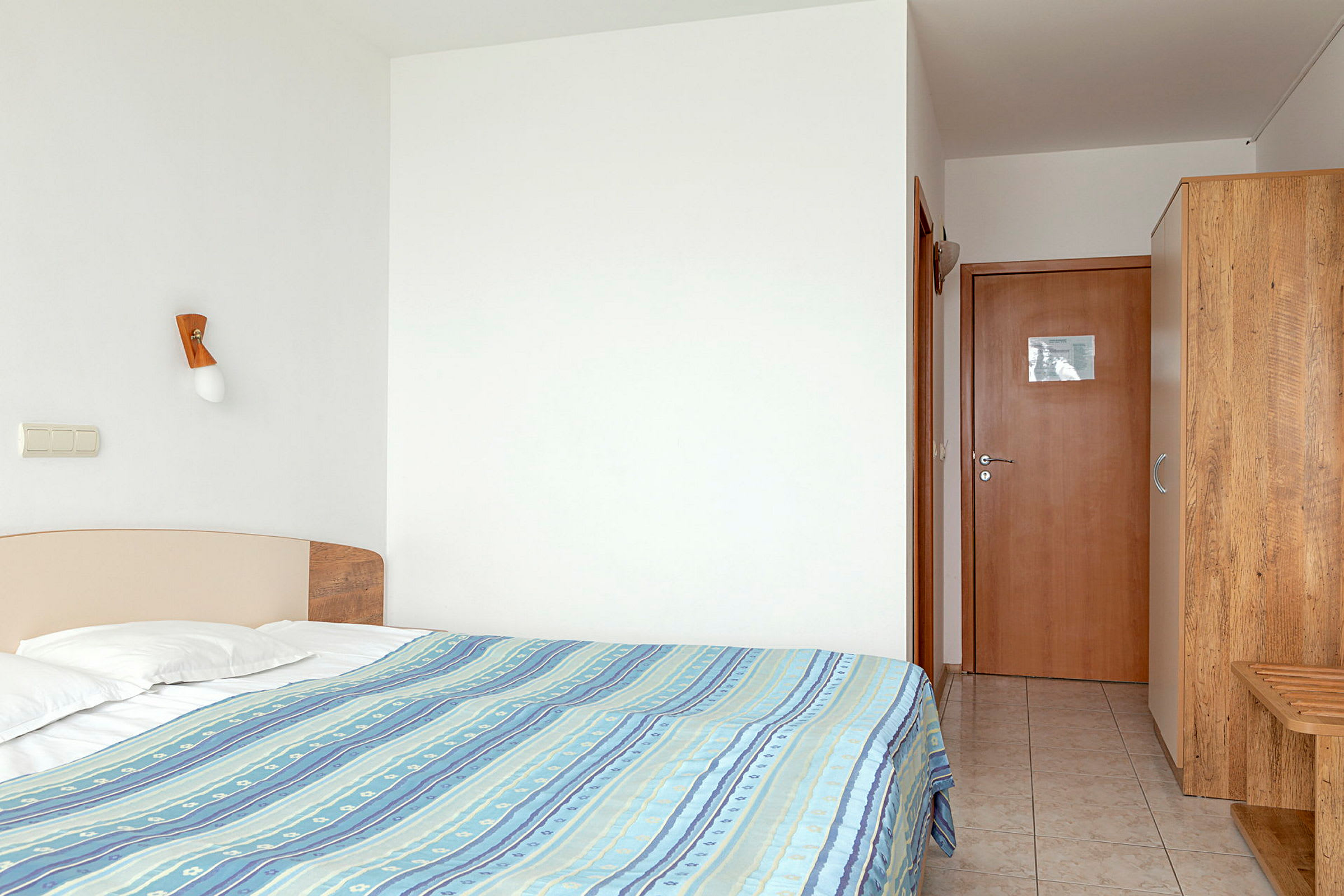 Hotellihuone, jossa vuode, vaatekaappi ja oviaukko. (Tekoälyn luoma teksti)