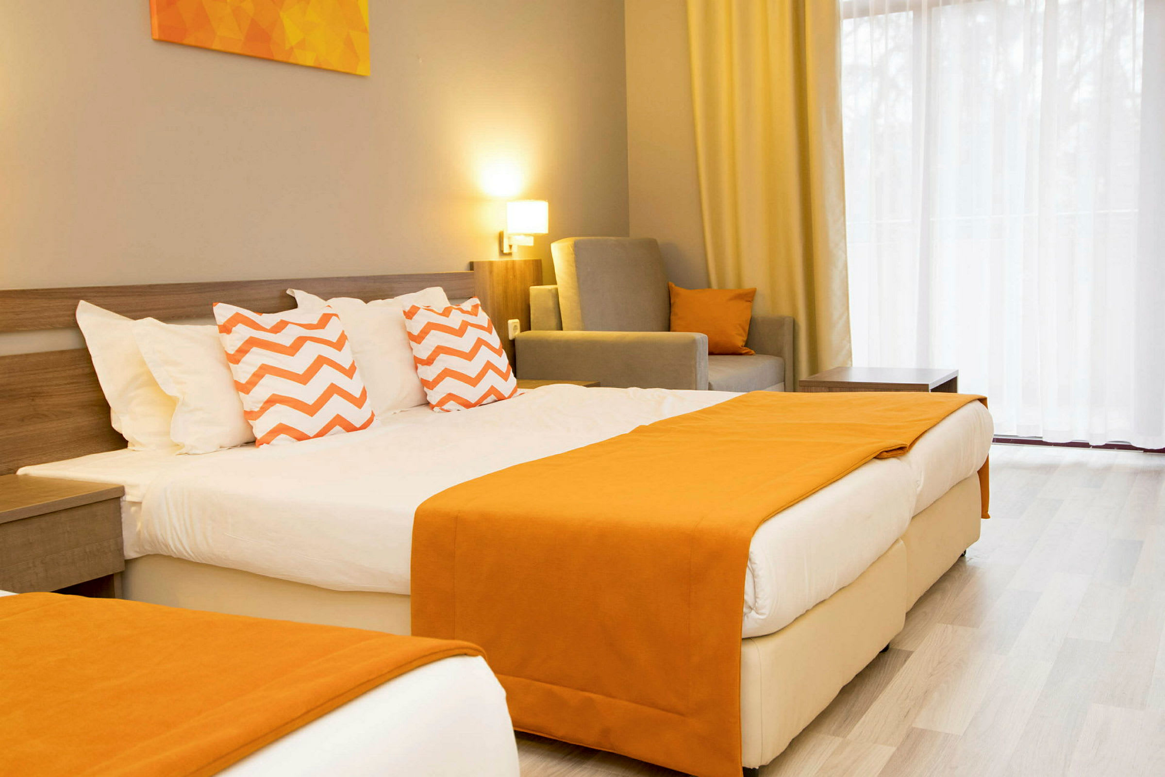 Hotellihuone, jossa parivuode, koristeltu oransseilla peitoilla ja siksak-kuvioisilla tyynyillä. (Tekoälyn luoma teksti)