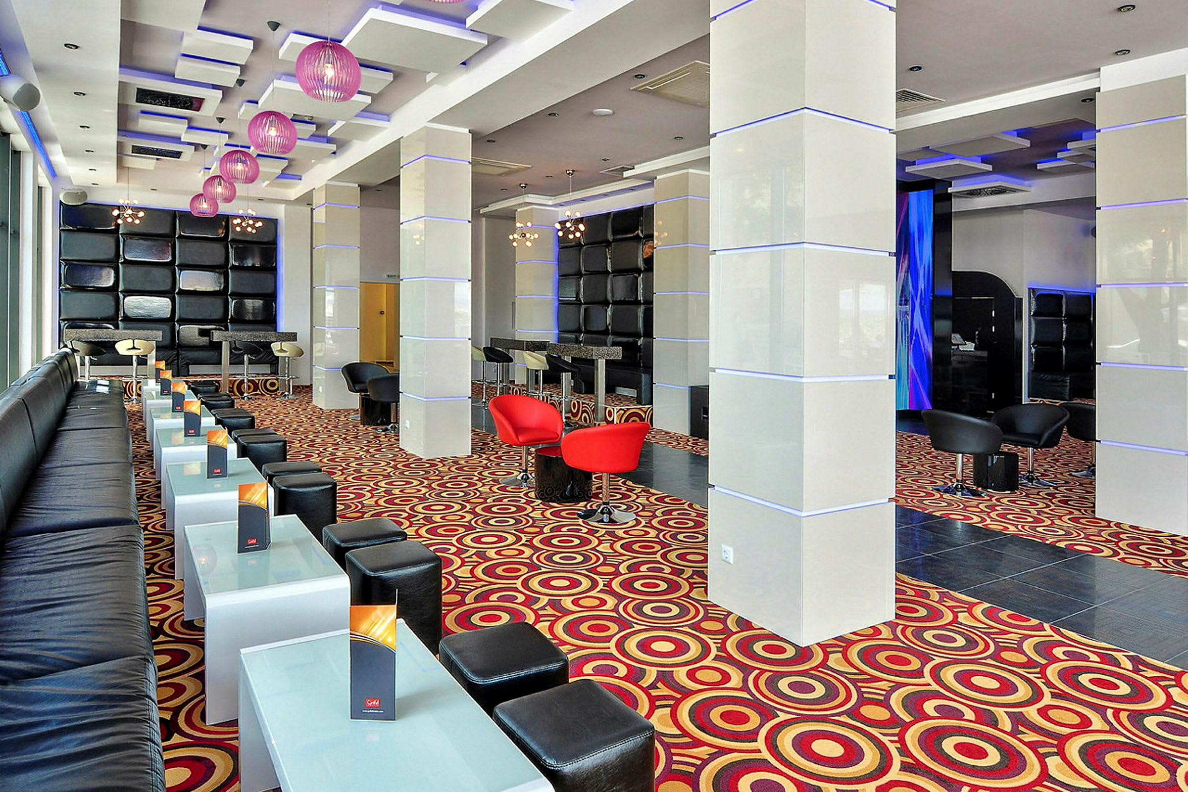 Moderni lounge, jossa istuimia, lasipöytiä ja värikäs matto. (Tekoälyn luoma teksti)