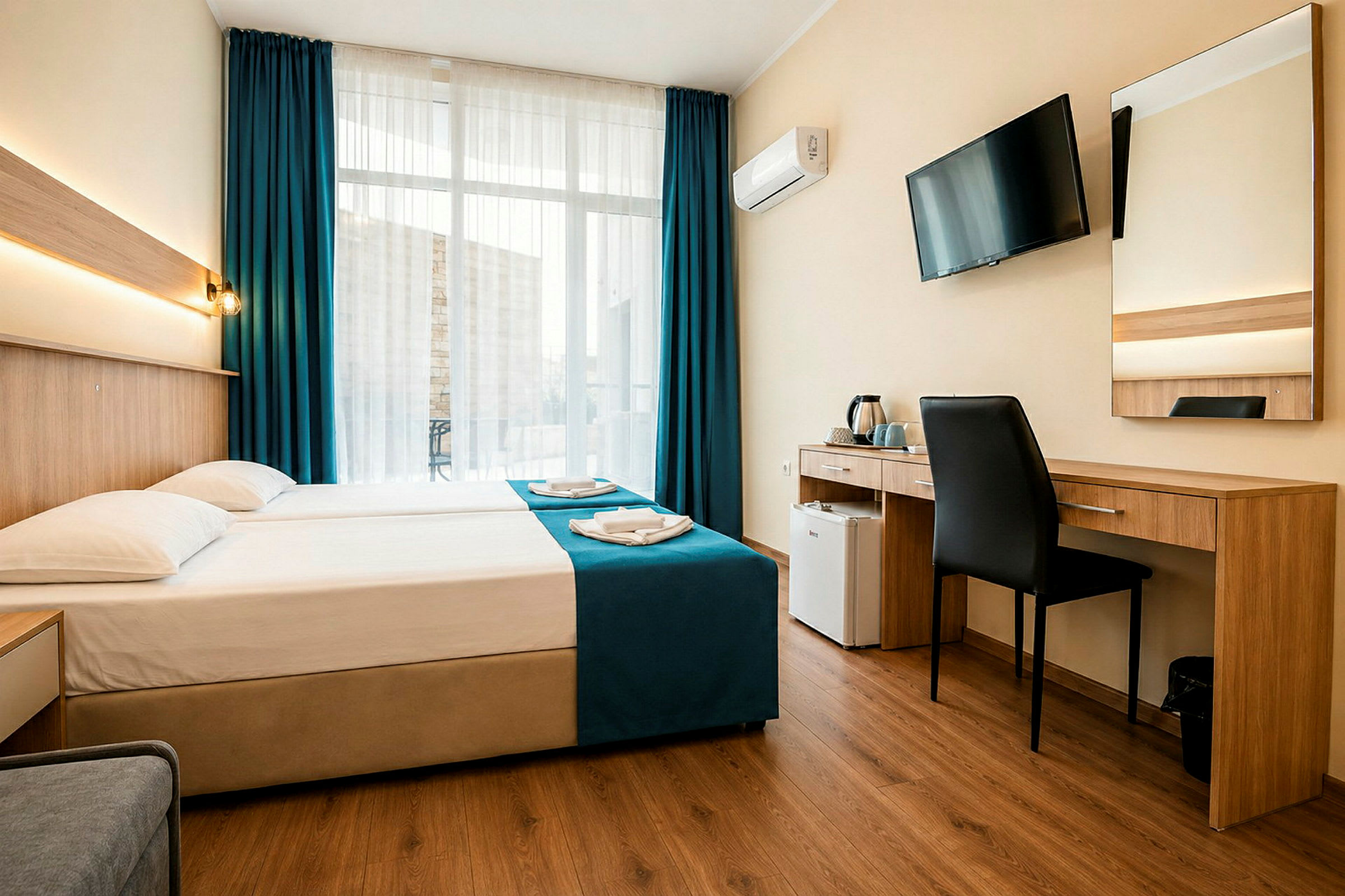 Hotellihuone, jossa on parivuode, työpöytä, tuoli, seinälle asennettu televisio ja suuret ikkunat tummansinisillä verhoilla. (Tekoälyn luoma teksti)
