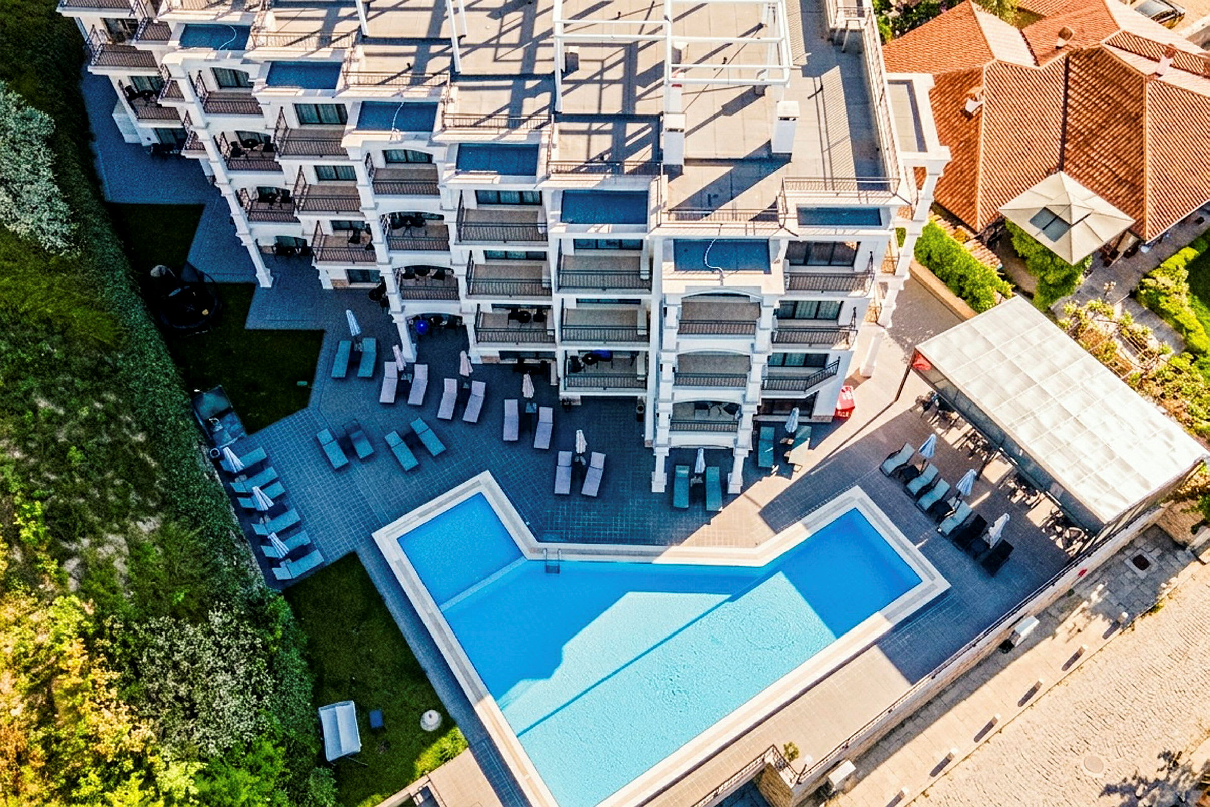 Ilmakuva hotellirakennuksesta, jossa on ulkouima-allas ja aurinkotuoleja. (Tekoälyn luoma teksti)