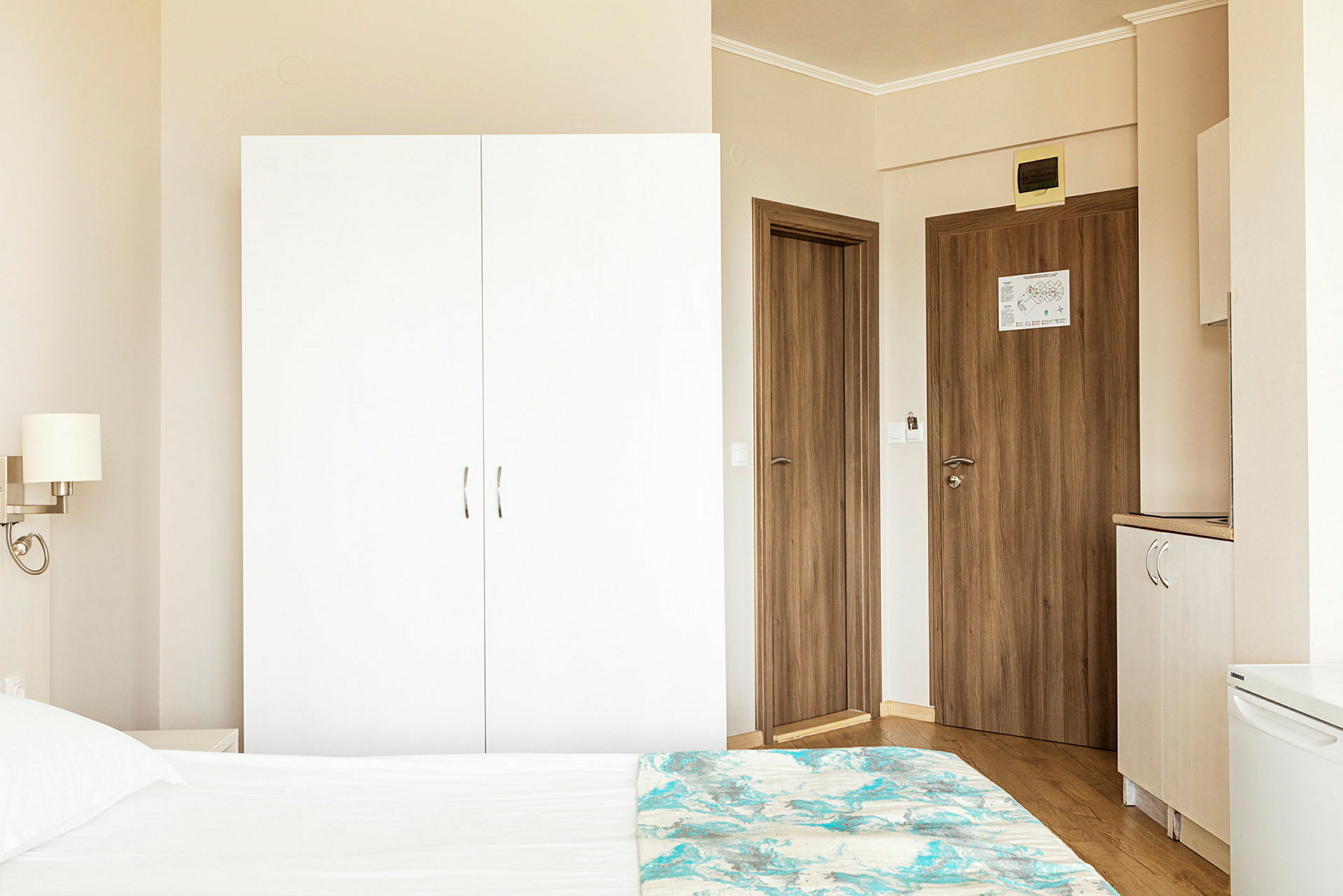 Hotellihuoneen ympäristö, jossa valkoinen vaatekaappi, puuovia ja osa sängystä etualalla. (Tekoälyn luoma teksti)