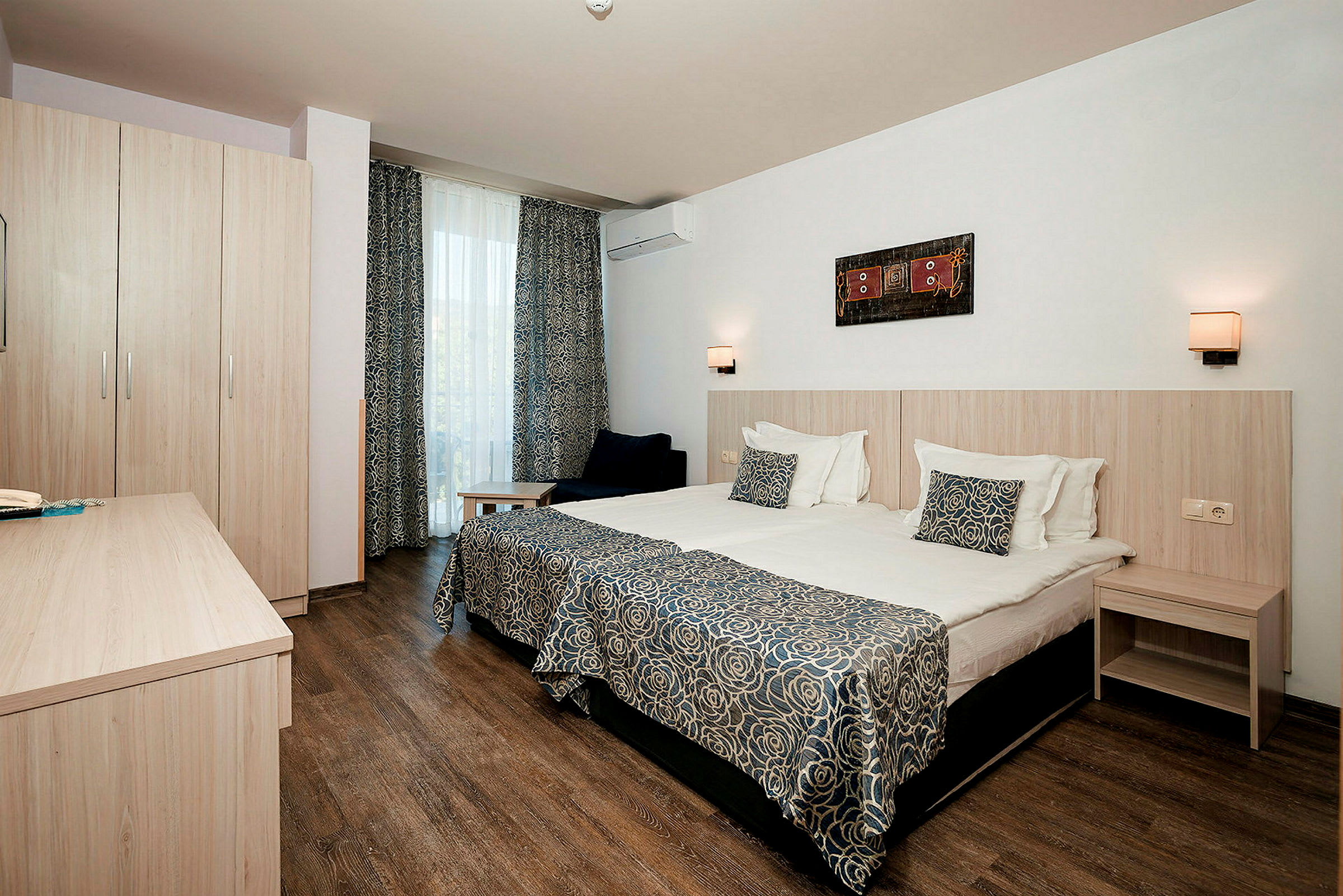 Hotellihuone, jossa on kaksi sänkyä, kirjoituspöytä, kaappi ja koristellut verhot. (Tekoälyn luoma teksti)