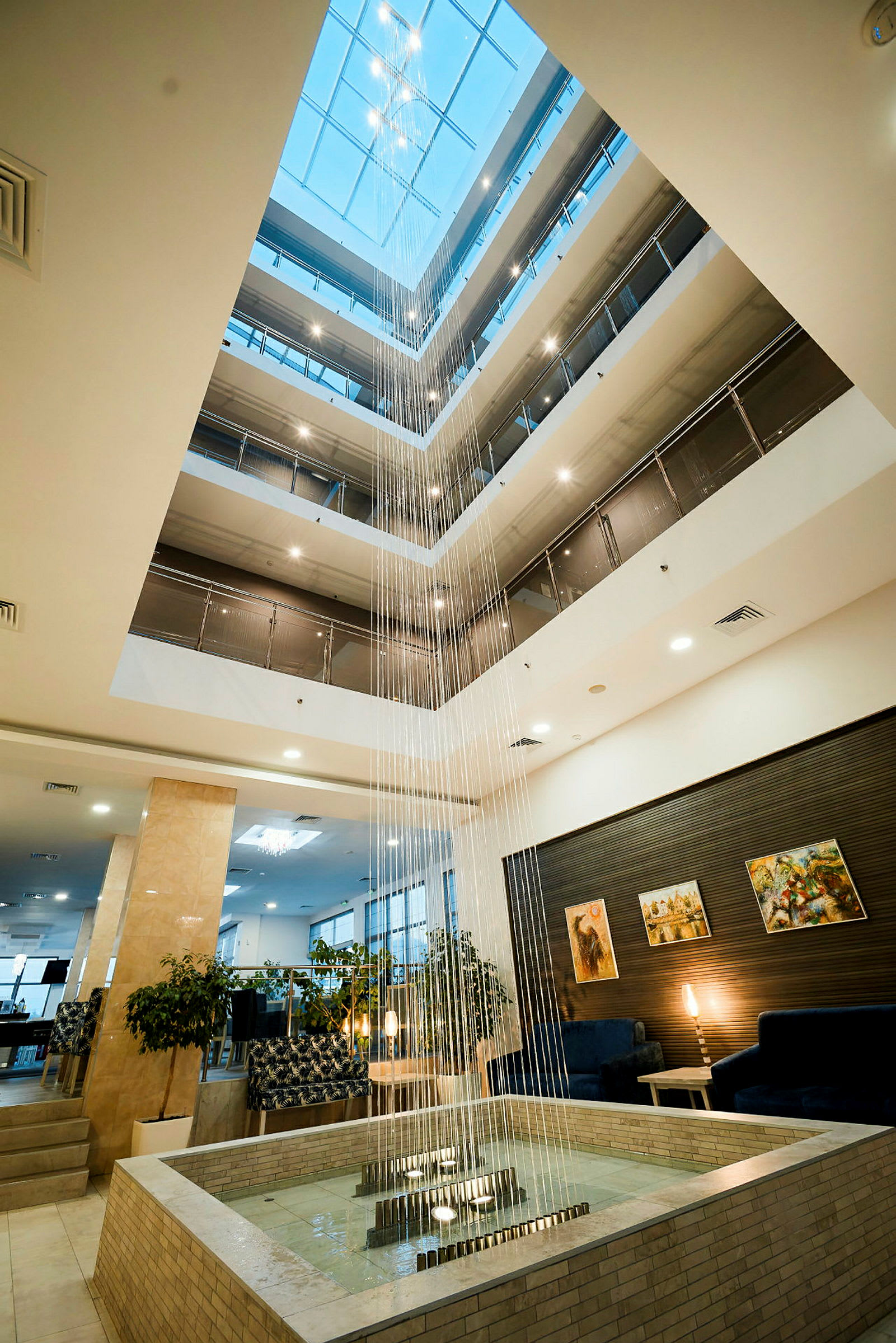 Valoisa ja tilava hotellin atrium, jossa on useita kerroksia, koristeltu keskellä olevalla vesiputouksella, joka virtaa suihkulähteeseen. (Tekoälyn luoma teksti)
