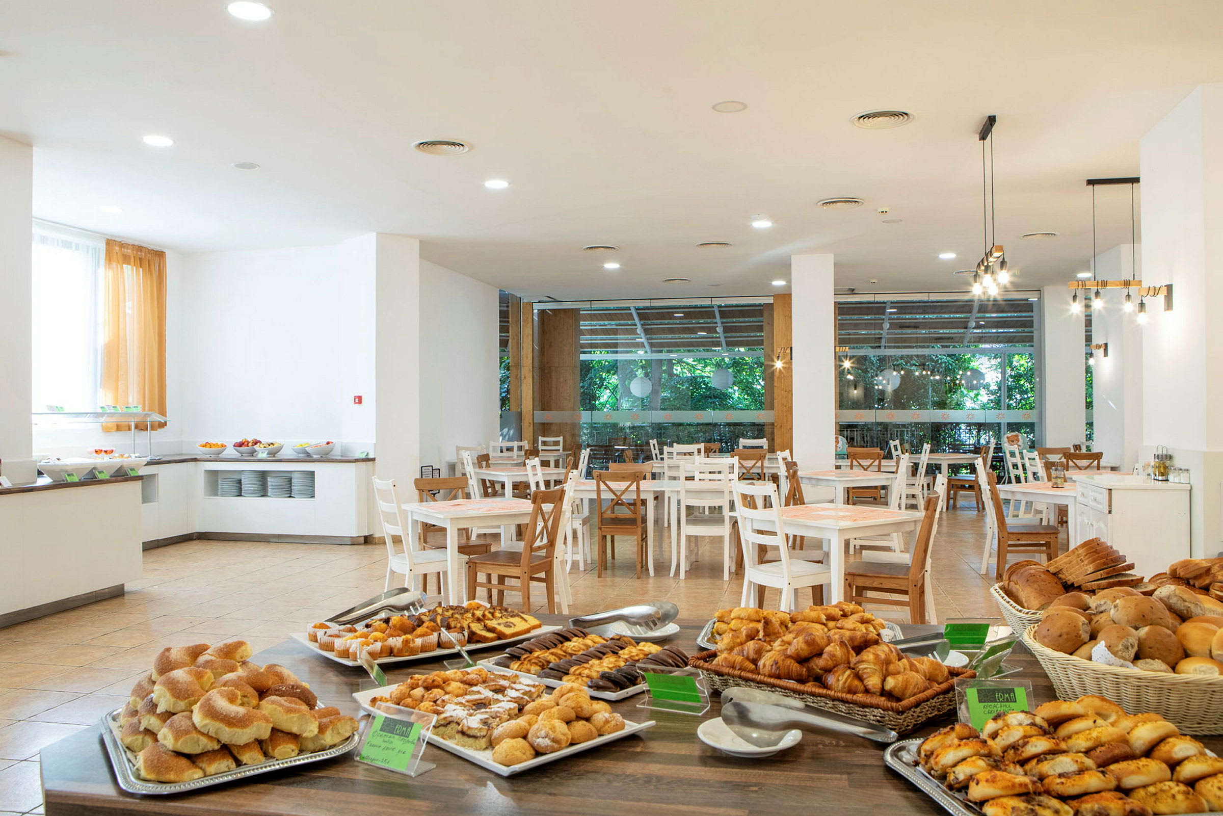 Hotellin ravintola-alue, jossa on pöytiä ja buffet täynnä erilaisia leipiä ja leivonnaisia. (Tekoälyn luoma teksti)
