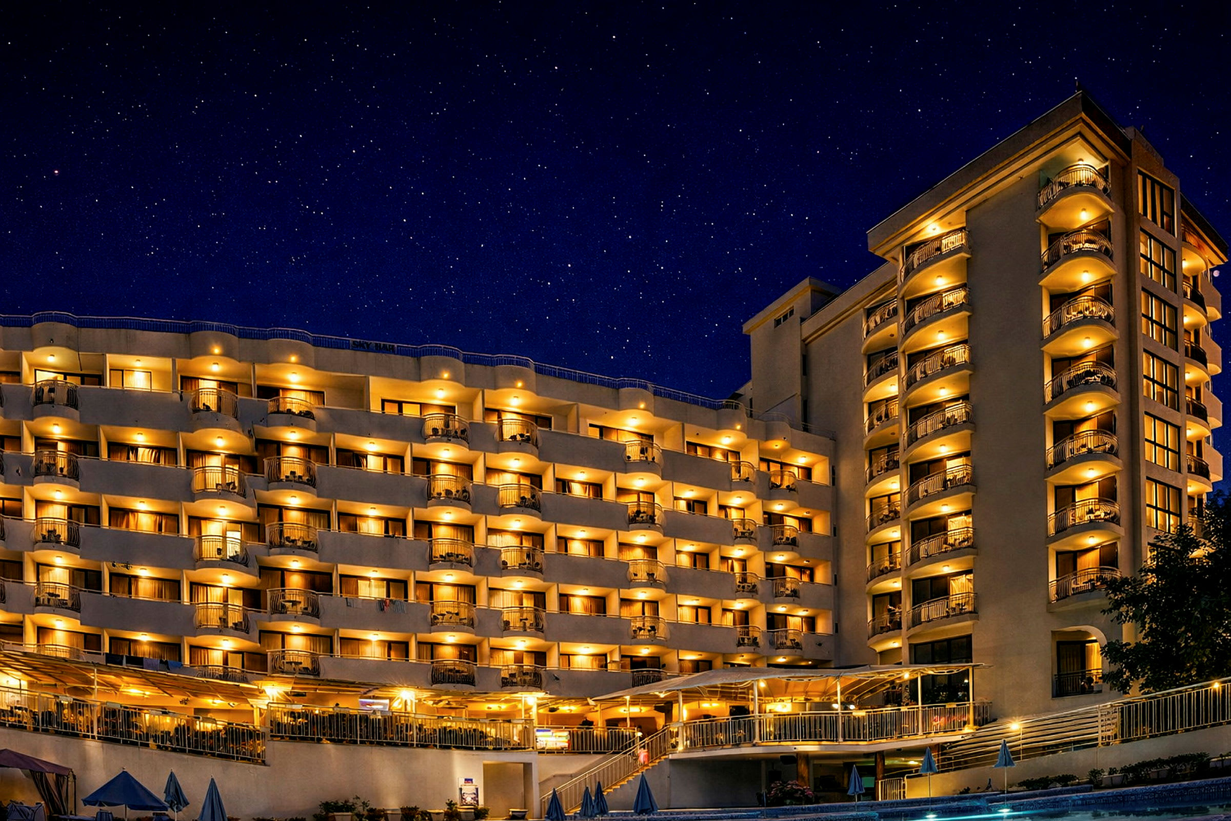 Hotellirakennus, jossa valaistuja parvekkeita ja ikkunoita tähtikirkkaan yötaivaan alla. (Tekoälyn luoma teksti)