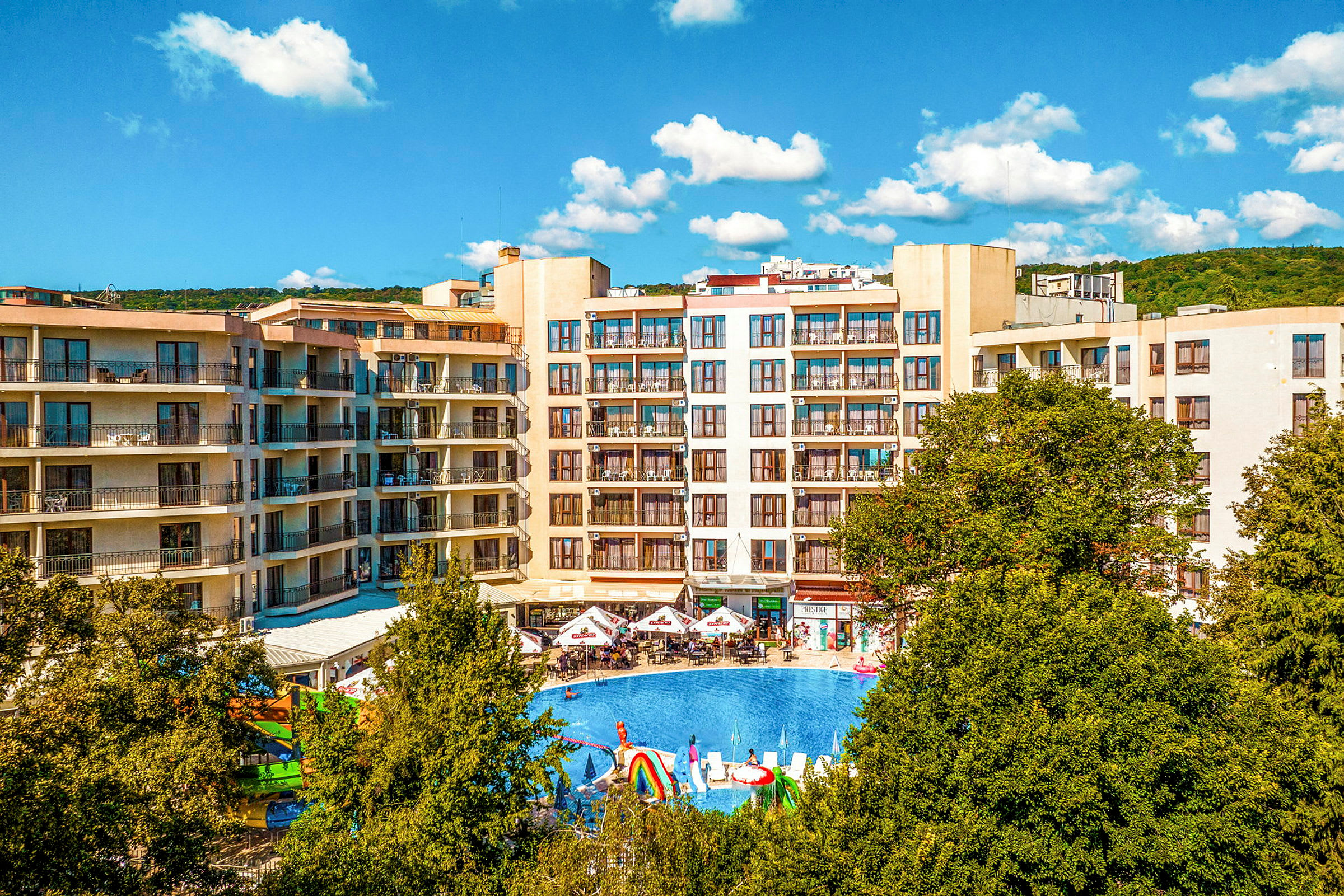 Hotellialue, jossa on kerrostaloja, suuri ulkouima-allas ja vihreitä puita etualalla. (Tekoälyn luoma teksti)