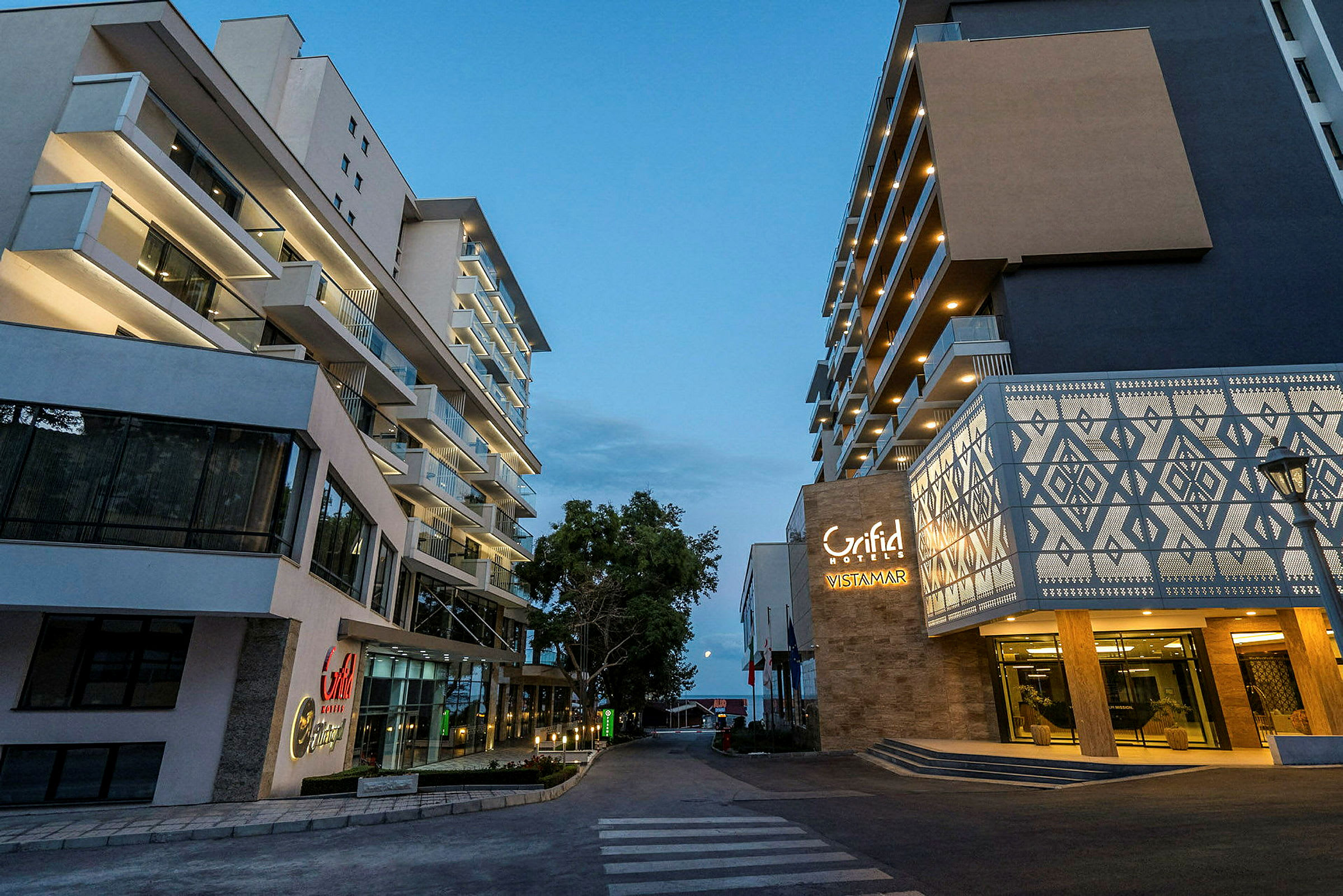 Kaksi modernia hotellirakennusta jalankulkutien vieressä illalla. (Tekoälyn luoma teksti)