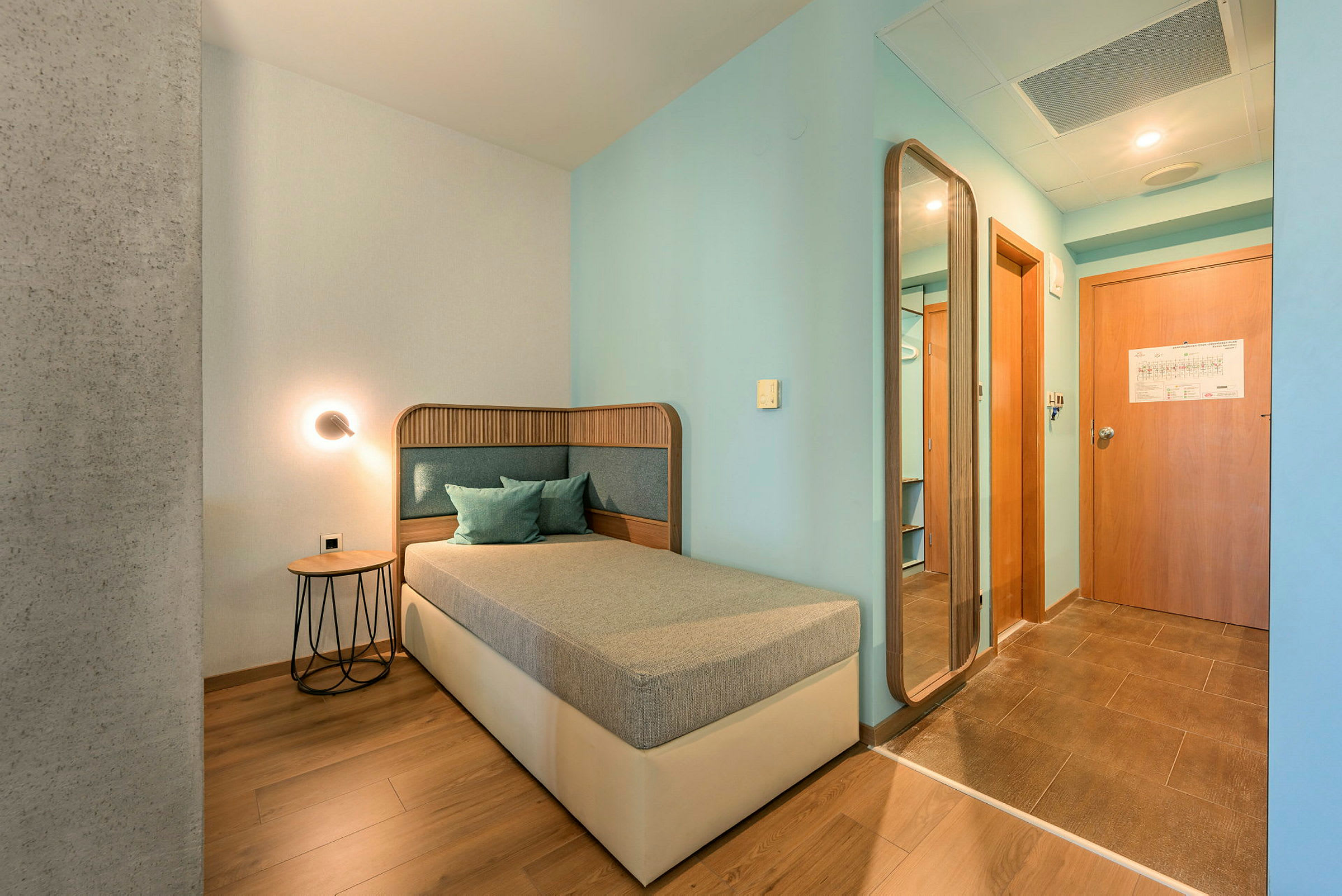 Hotellihuone, jossa on yhden hengen sänky, pöytä ja peili. (Tekoälyn luoma teksti)