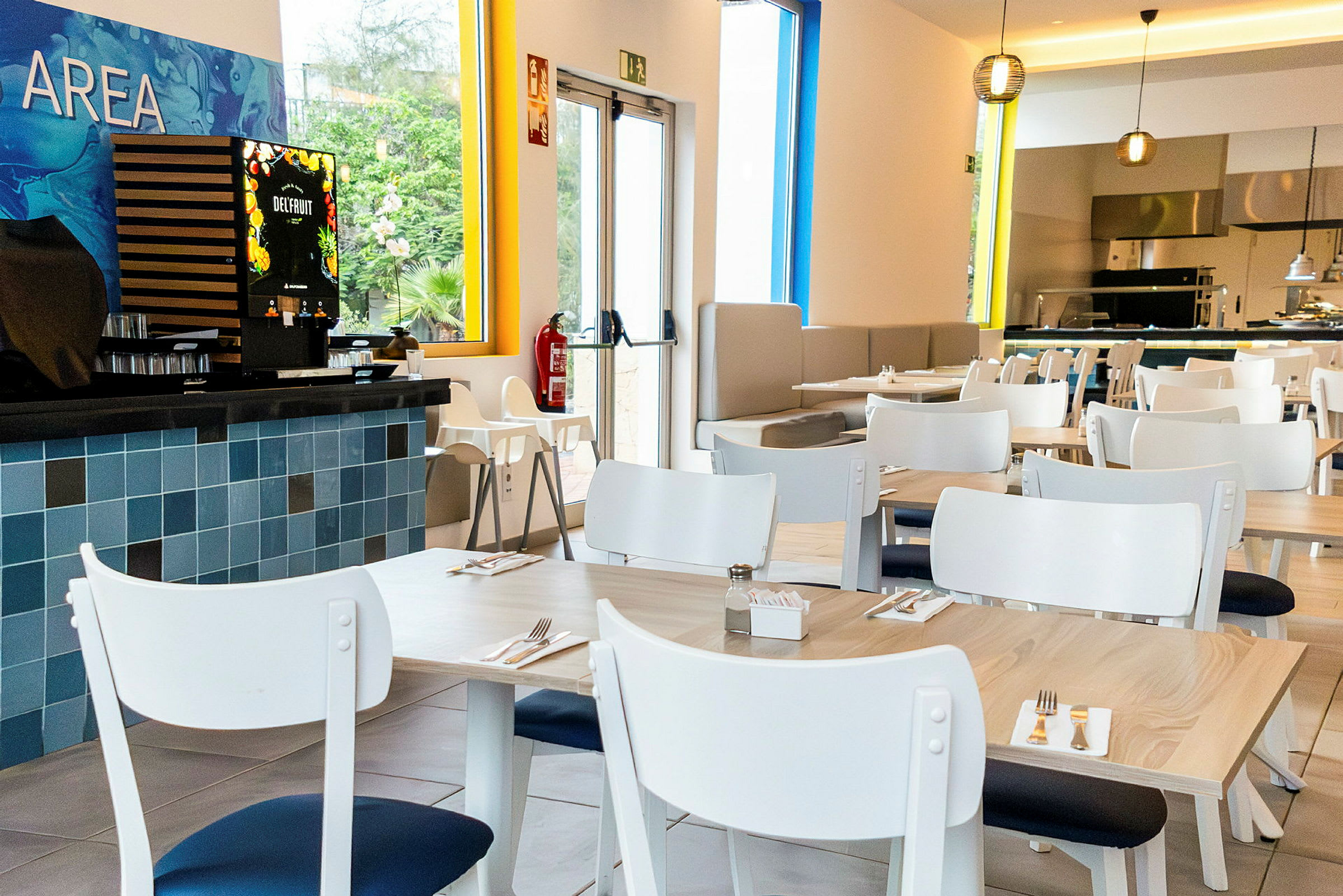 Moderni ravintola, jossa on valkoiset pöydät ja tuolit. Vasemmalla näkyy mehulaite. (Tekoälyn luoma teksti)