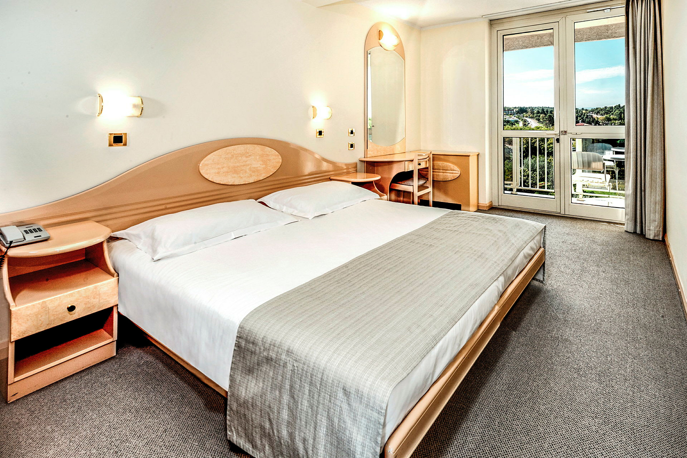 Hotellihuone, jossa on parisänky, yöpöytä, kirjoituspöytä ja parveke näkymillä. (Tekoälyn luoma teksti)