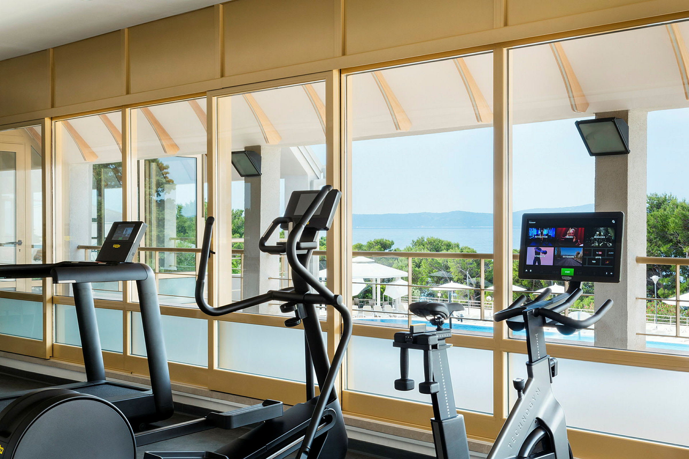 Kuntosali, jossa harjoituslaitteita, suuret ikkunat näkymällä merelle. (Tekoälyn luoma teksti)