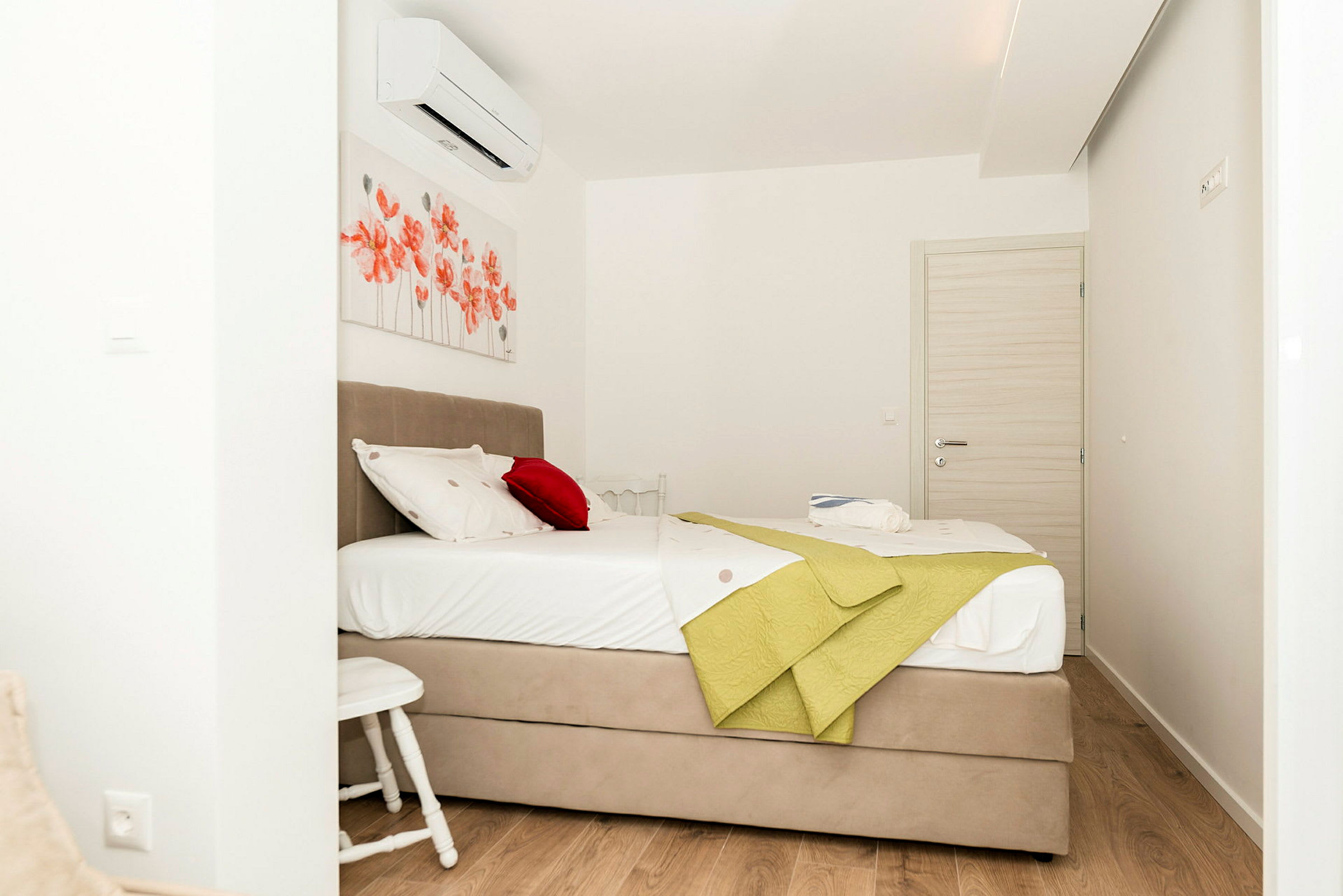 Hotellihuone, jossa on pedattu sänky, punaisia kukkaisia seinäkoristeita ja vaaleat huonekalut. (Tekoälyn luoma teksti)