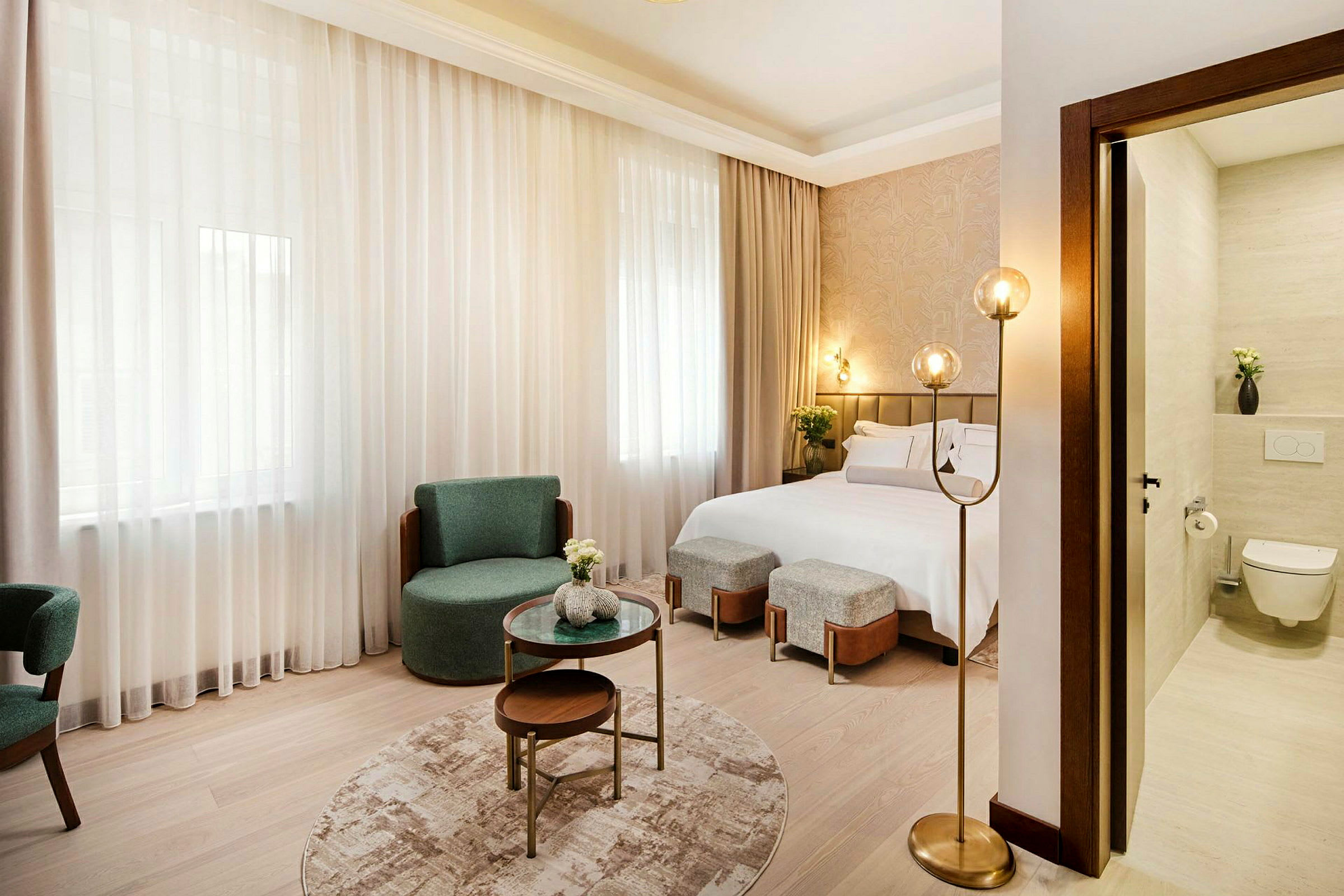 Moderni hotellihuone, jossa on parivuode, tuolit, sohvapöytä ja osittain näkyvä kylpyhuoneosio. (Tekoälyn luoma teksti)