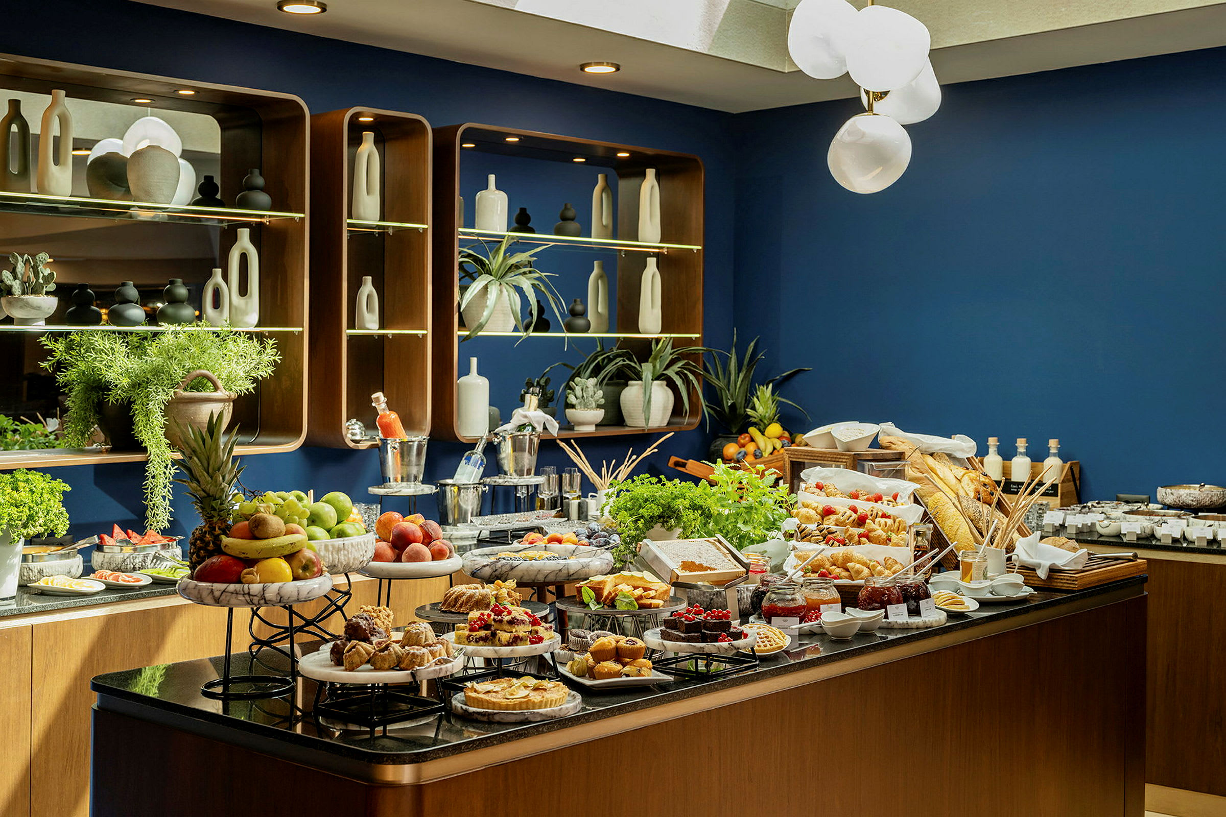 Buffet, jossa on erilaisia ruokia, kuten hedelmiä, leivonnaisia ja salaatteja, sekä koristeellisia hyllyjä taustalla. (Tekoälyn luoma teksti)