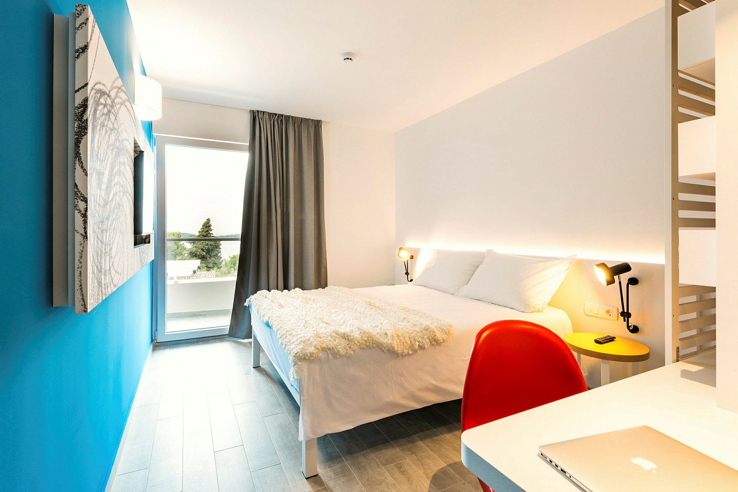 Modernisti sisustettu hotellihuone, jossa parivuode, kirjoituspöytä ja sininen seinä. (Tekoälyn luoma teksti)