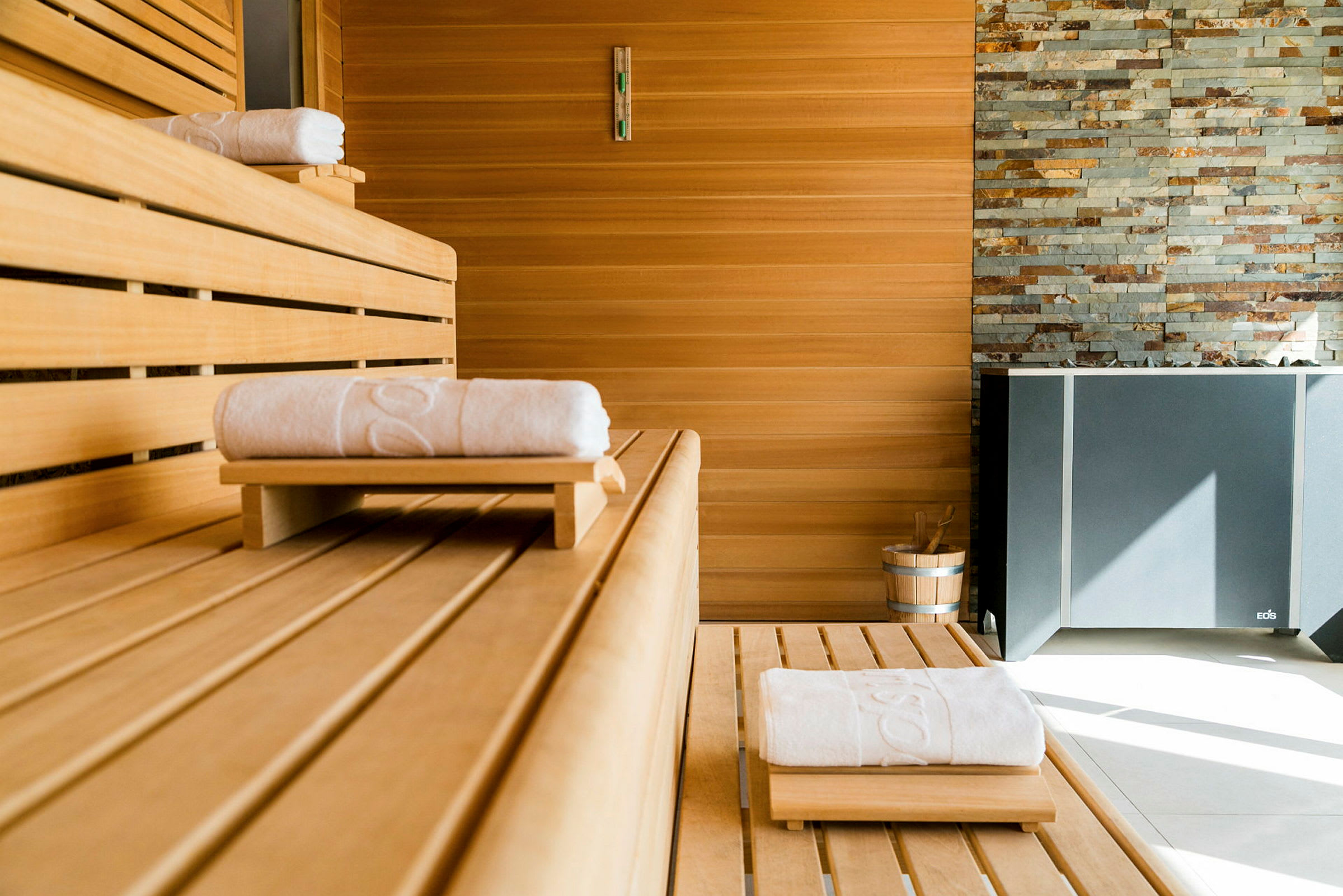 Sauna, jossa on vaaleat puupaneelit, pyyhkeet puupinnoilla ja ämpäri nurkassa. (Tekoälyn luoma teksti)