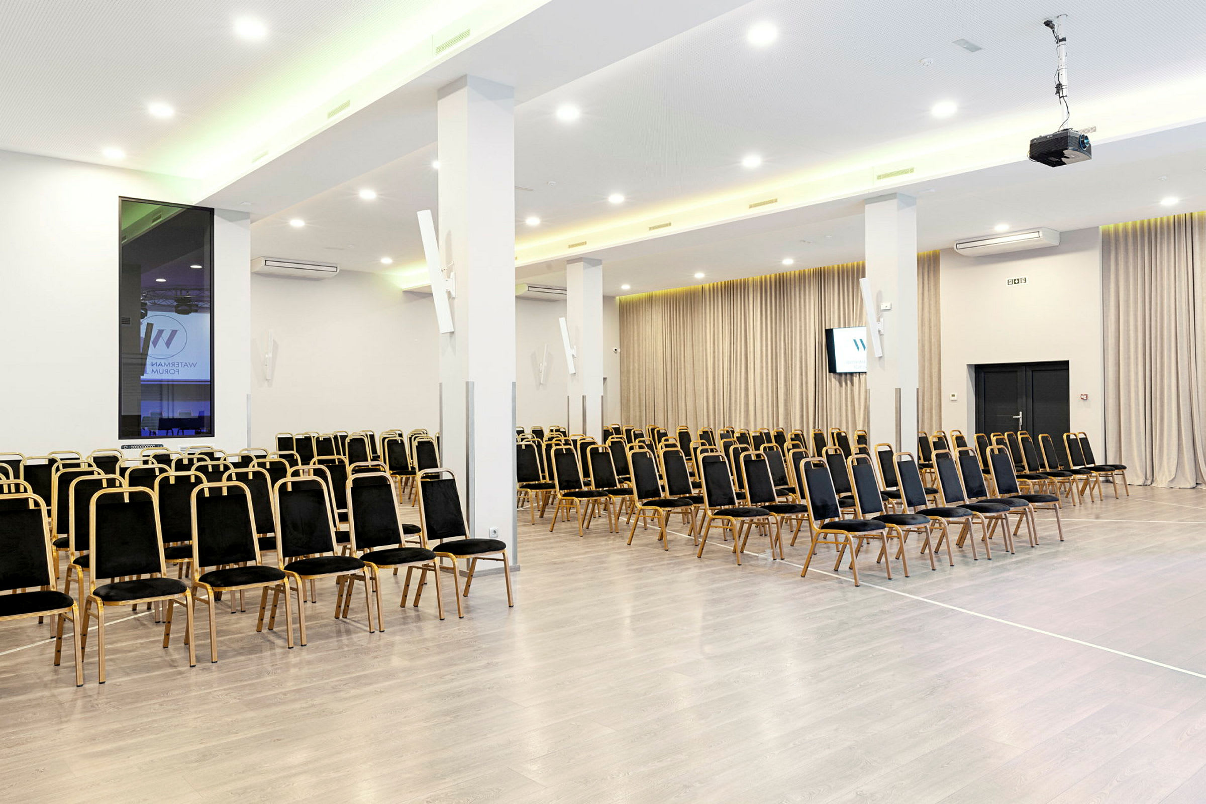 Konferenssihuone, jossa useita rivejä tyhjiä tuoleja ja projektiojärjestelmä. (Tekoälyn luoma teksti)