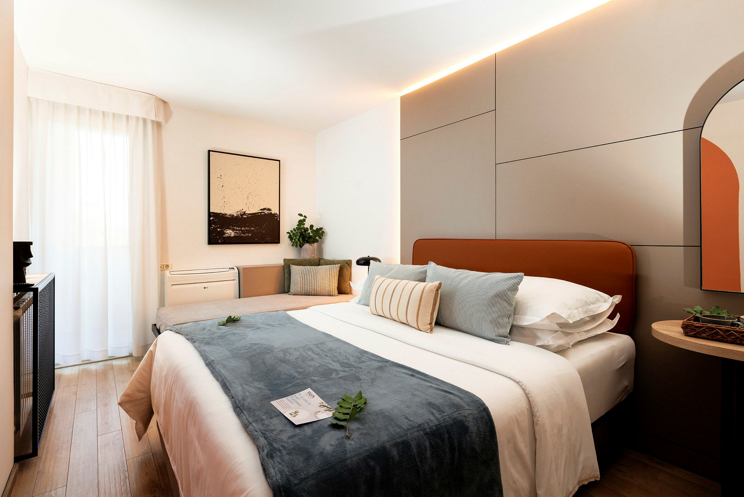 Moderni hotellihuone, jossa iso sänky, tyynyjä ja sisustuselementtejä. (Tekoälyn luoma teksti)