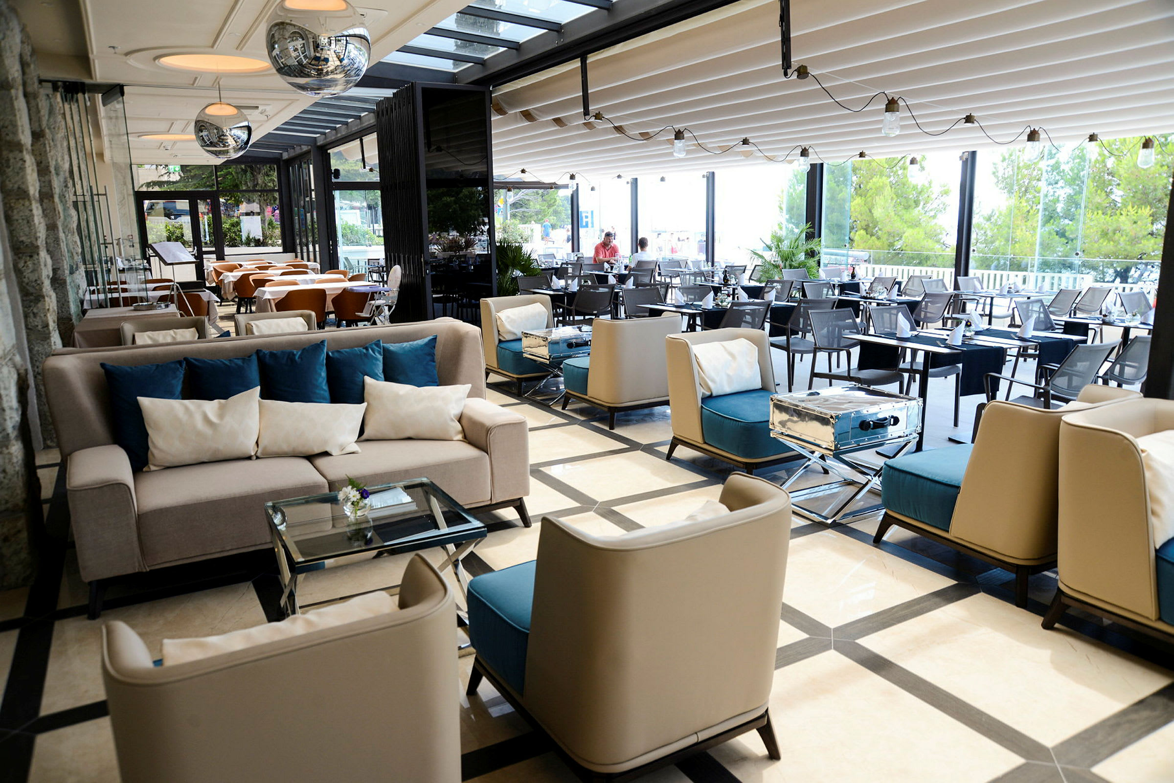 Moderni lounge-alue, jossa on sohvia, istumapaikkoja ja pöytiä. Suuret ikkunat näkymällä puutarhaan. (Tekoälyn luoma teksti)