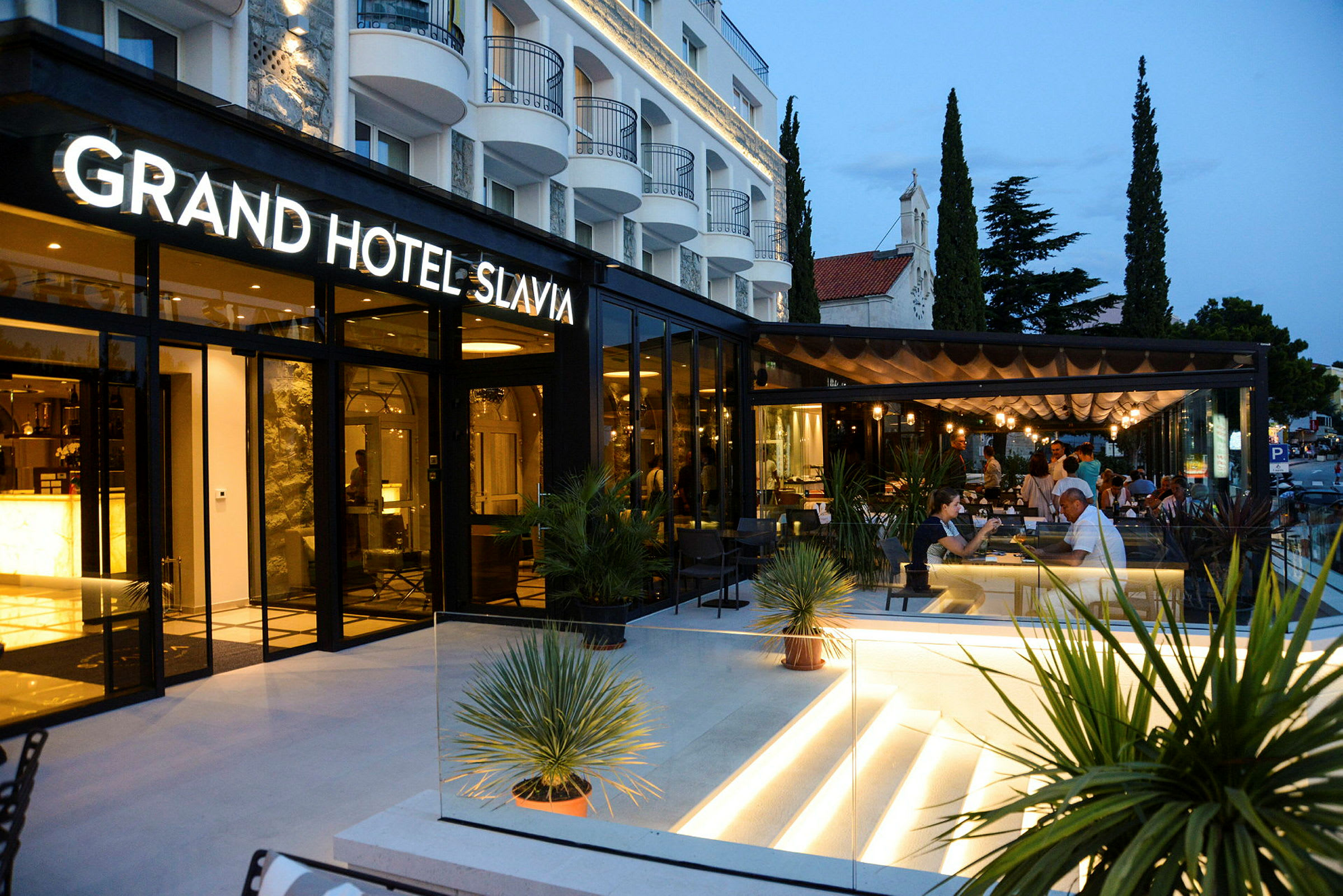 Grand Hotel Slavia, jossa on moderni ulkoterassi ja iltavalaistus. (Tekoälyn luoma teksti)