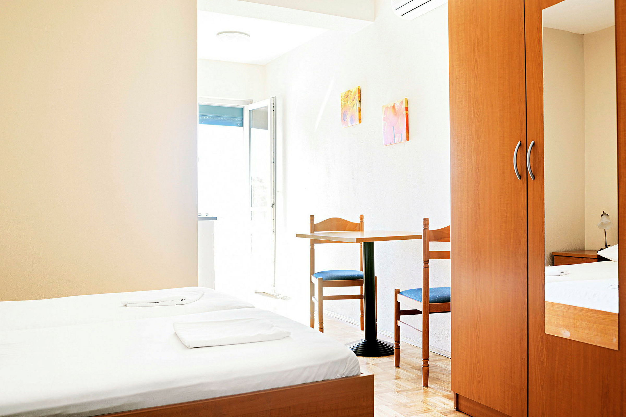 Hotellihuone, jossa kaksi erillistä vuodetta, pöytä ja kaksi tuolia sekä vaatekaappi. (Tekoälyn luoma teksti)