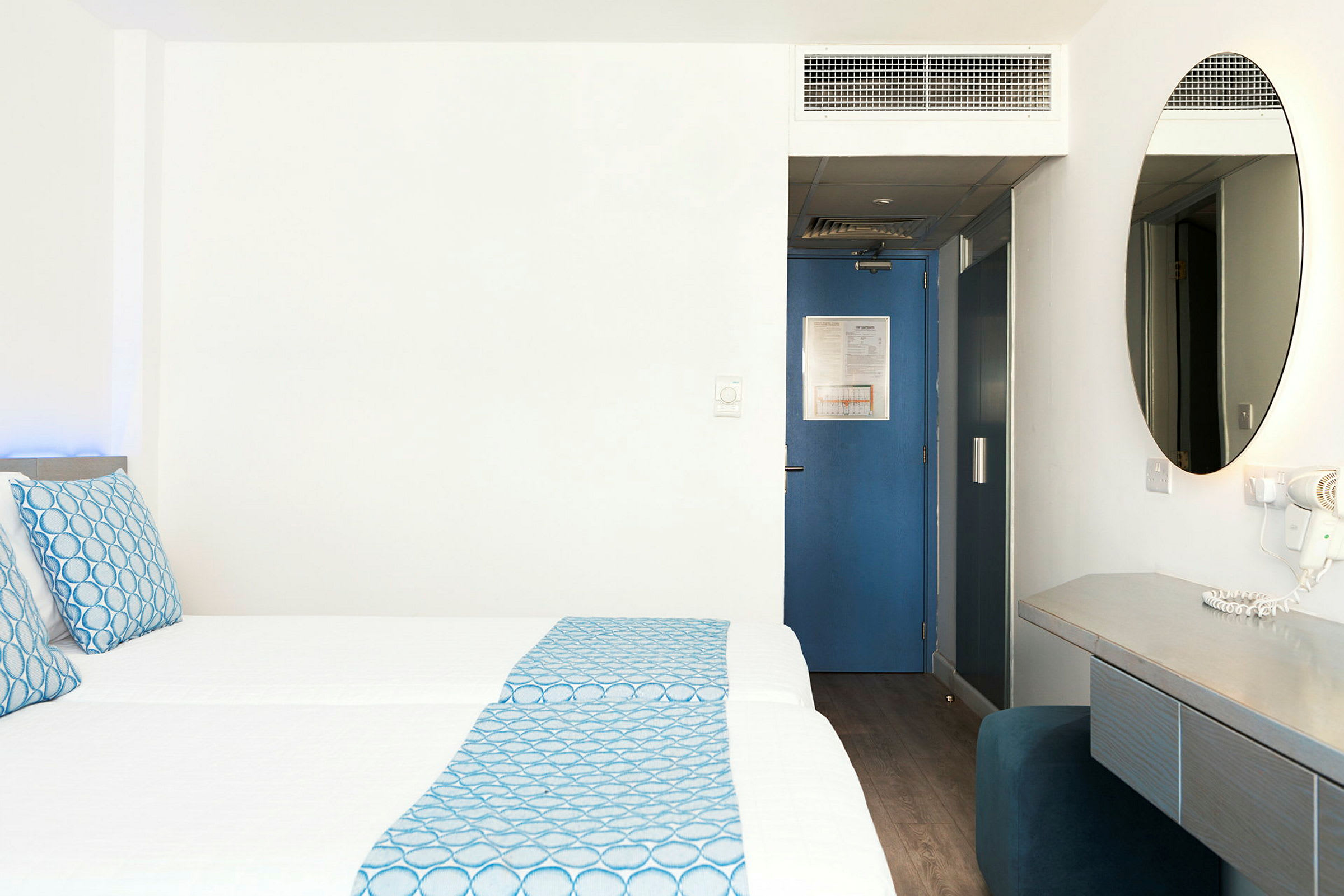 Hotellihuone, jossa kaksi vuodetta, sinisiä yksityiskohtia ja kirjoituspöytä. (Tekoälyn luoma teksti)