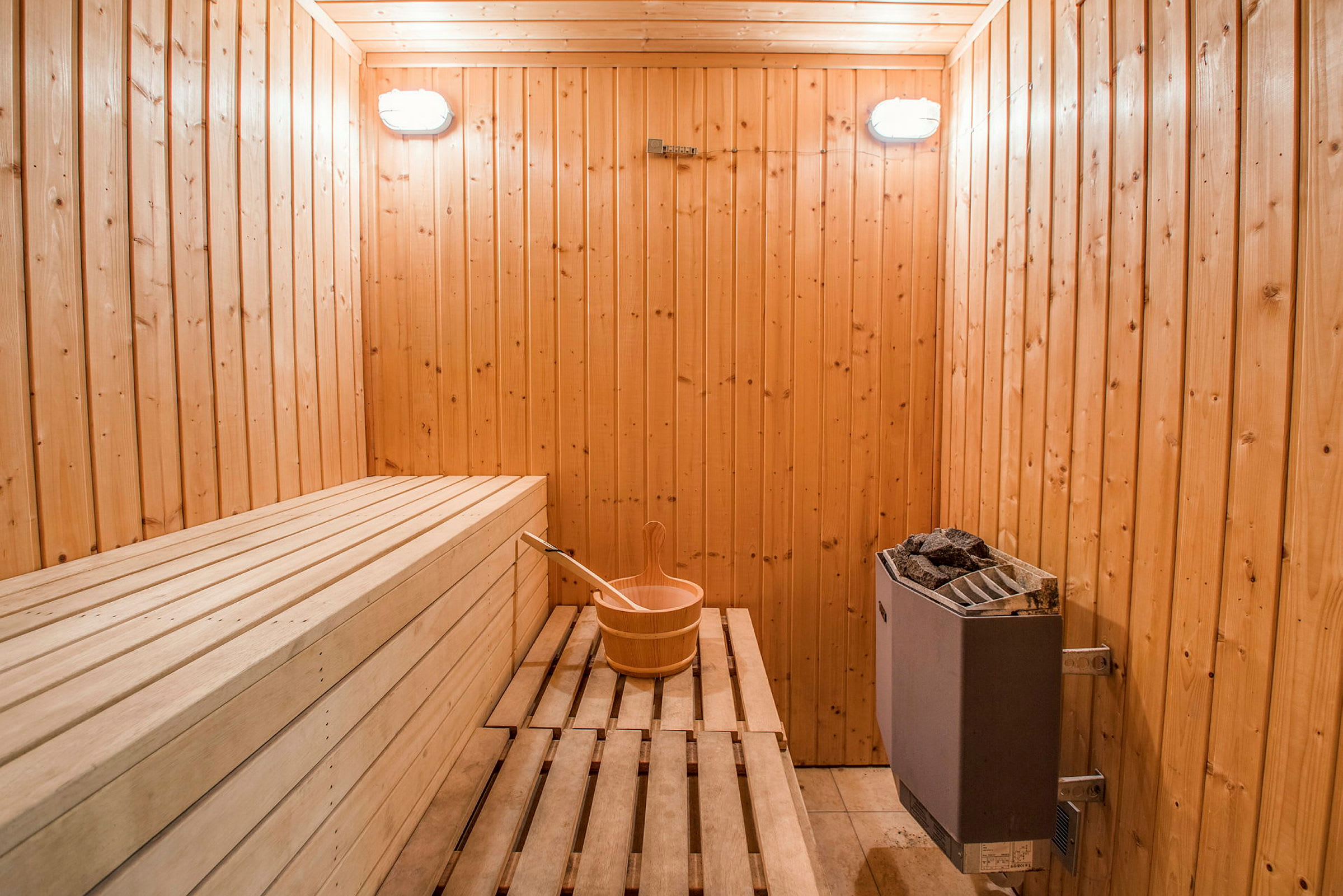 Sauna, jossa on puupanelit, penkit, ämpäri kauhalla ja kiuas. (Tekoälyn luoma teksti)