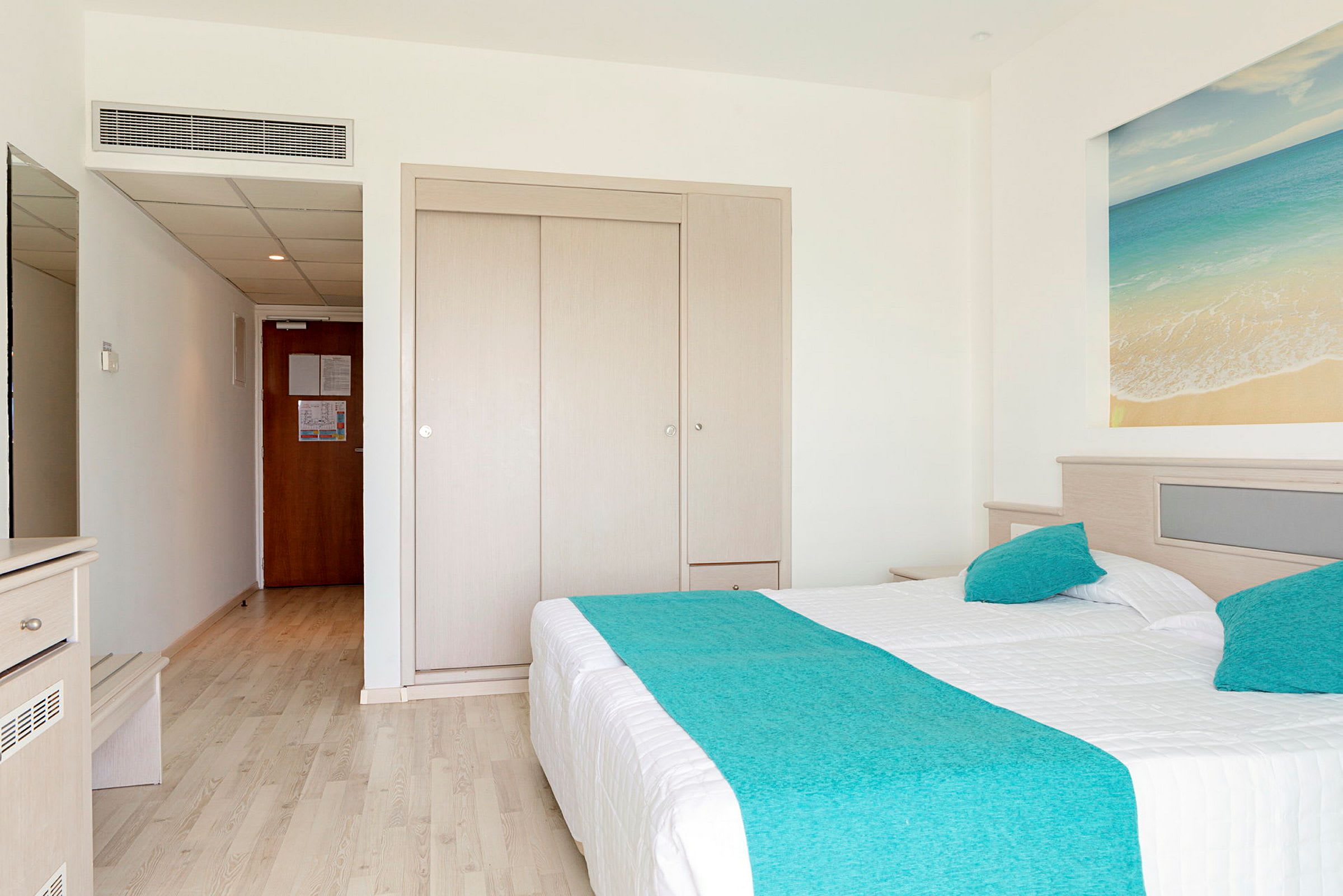 Hotellihuone, jossa parivuode ja sininen sängynpeite. (Tekoälyn luoma teksti)