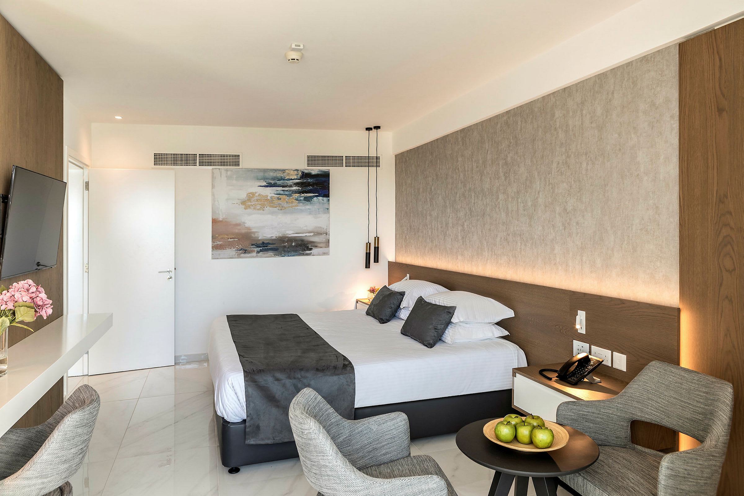 Hotellihuone, jossa on parivuode, istuinryhmä ja taidetta seinällä. (Tekoälyn luoma teksti)