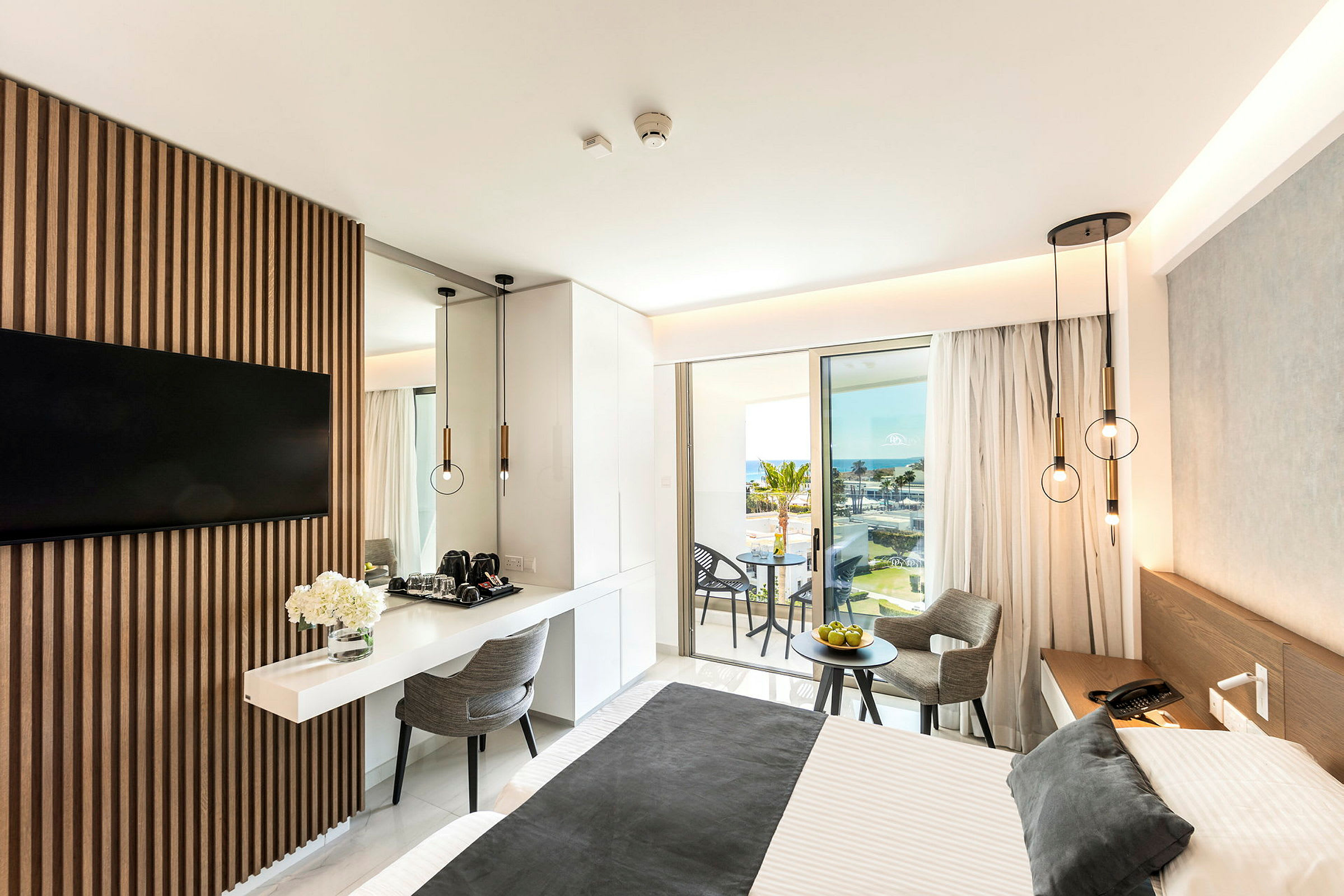 Moderni hotellihuone, jossa on parivuode, pöytä ja tuolit sekä merinäköala parvekkeelta. (Tekoälyn luoma teksti)
