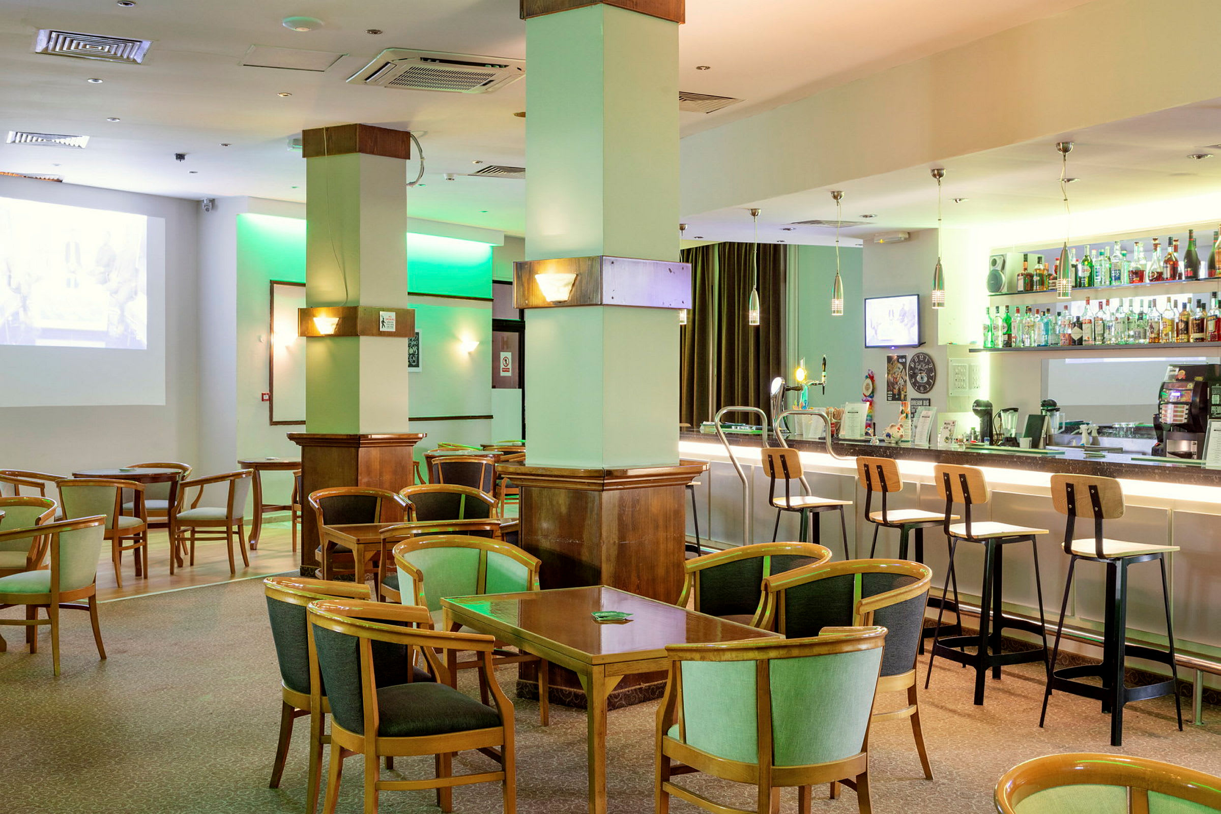 Hotellibaari, jossa istumapaikkoja ja pöytiä sekä hyllyt täynnä pulloja baaritiskin takana. (Tekoälyn luoma teksti)
