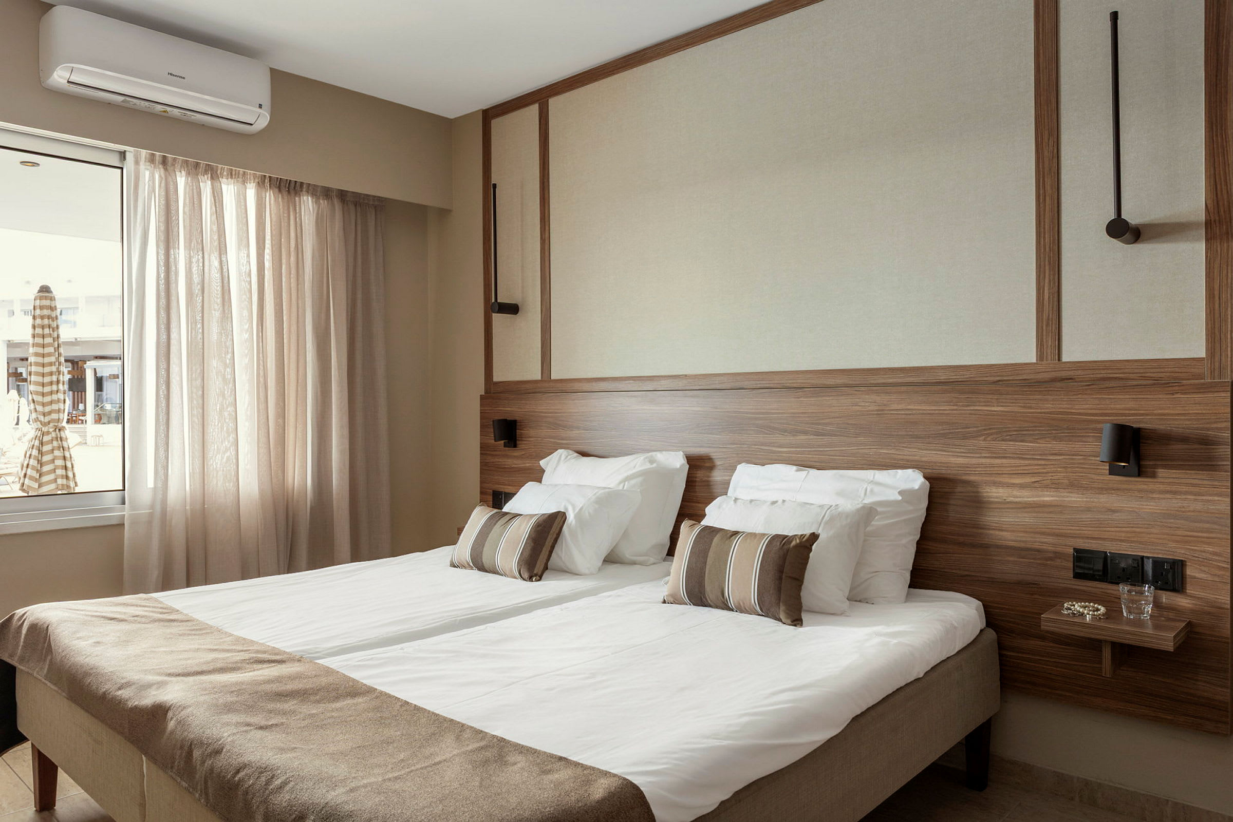 Hotellihuone, jossa parivuode, vaaleat verhot, puupaneelit ja ikkuna näköalalla. (Tekoälyn luoma teksti)