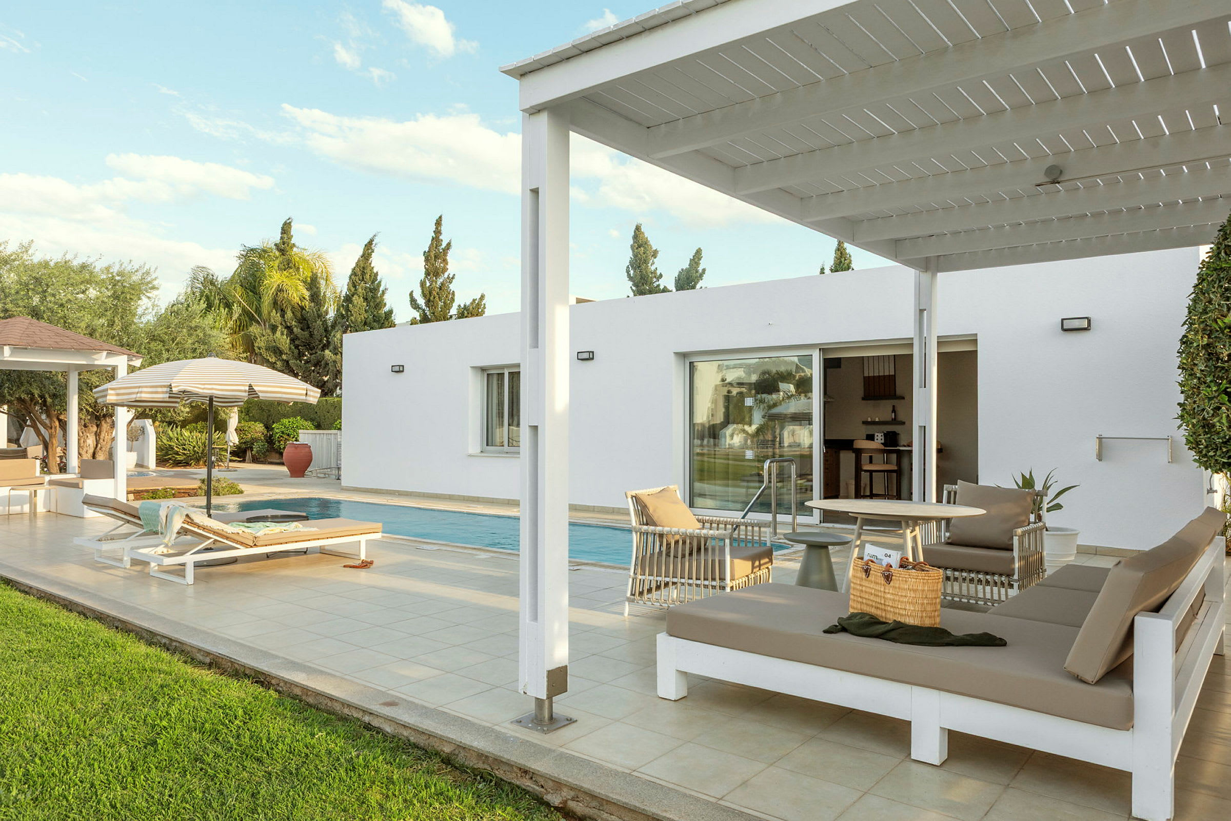 Ulkotila, jossa on uima-allas, aurinkotuolit ja pergola modernin rakennuksen vieressä. (Tekoälyn luoma teksti)