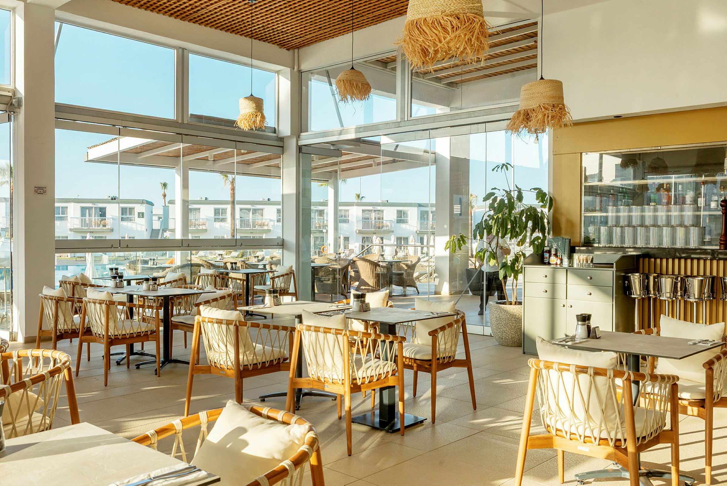 Ravintola, jossa on suuret ikkunat ja puiset tuolit pöytien ympärillä. (Tekoälyn luoma teksti)