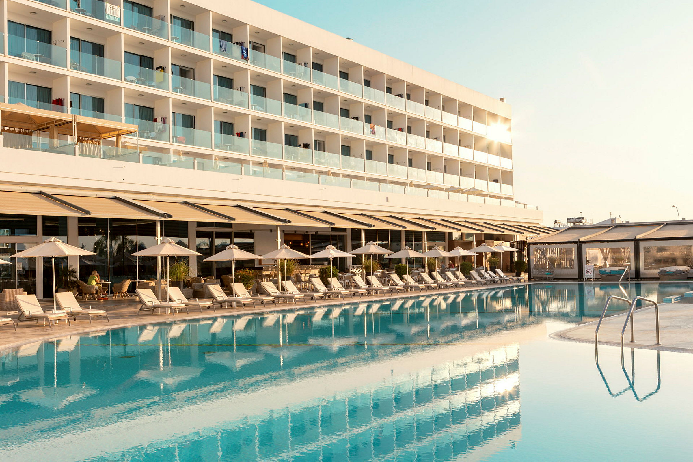 Hotellirakennus parvekkeiden kera näkyy uima-altaan ja aurinkotuolien takana. (Tekoälyn luoma teksti)