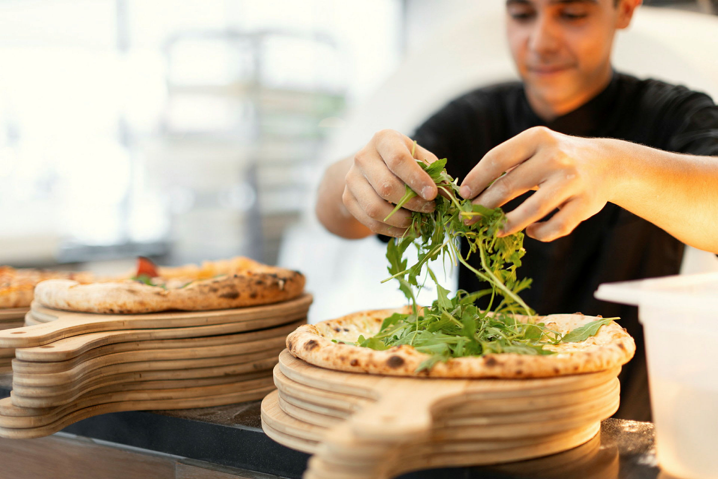Henkilö lisää rucolaa pizzan päälle. (Tekoälyn luoma teksti)