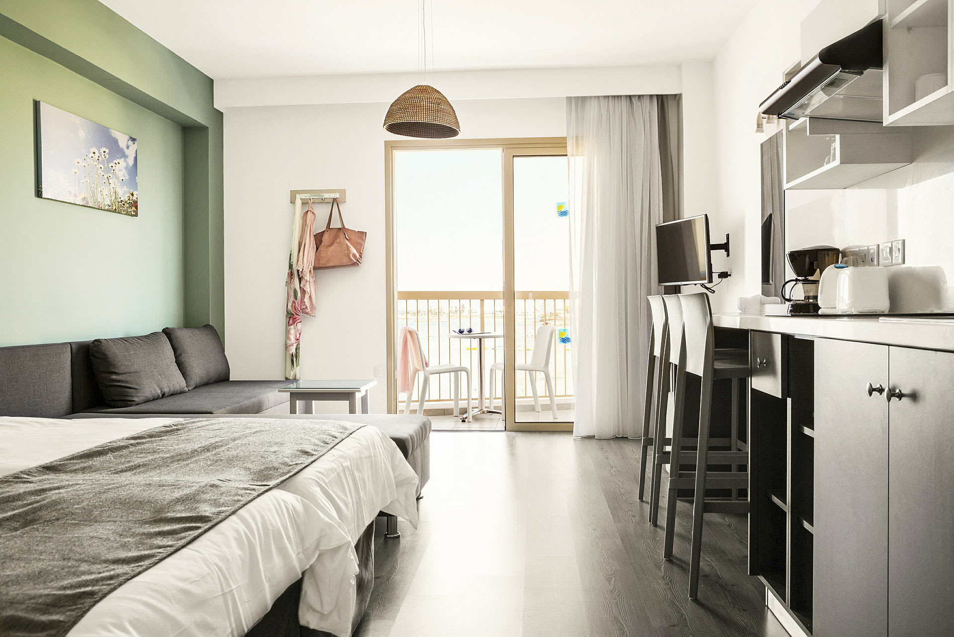 Moderni hotellihuone, jossa on vuodesohva, sänky, keittiövälineet ja parveke näköalalla. (Tekoälyn luoma teksti)