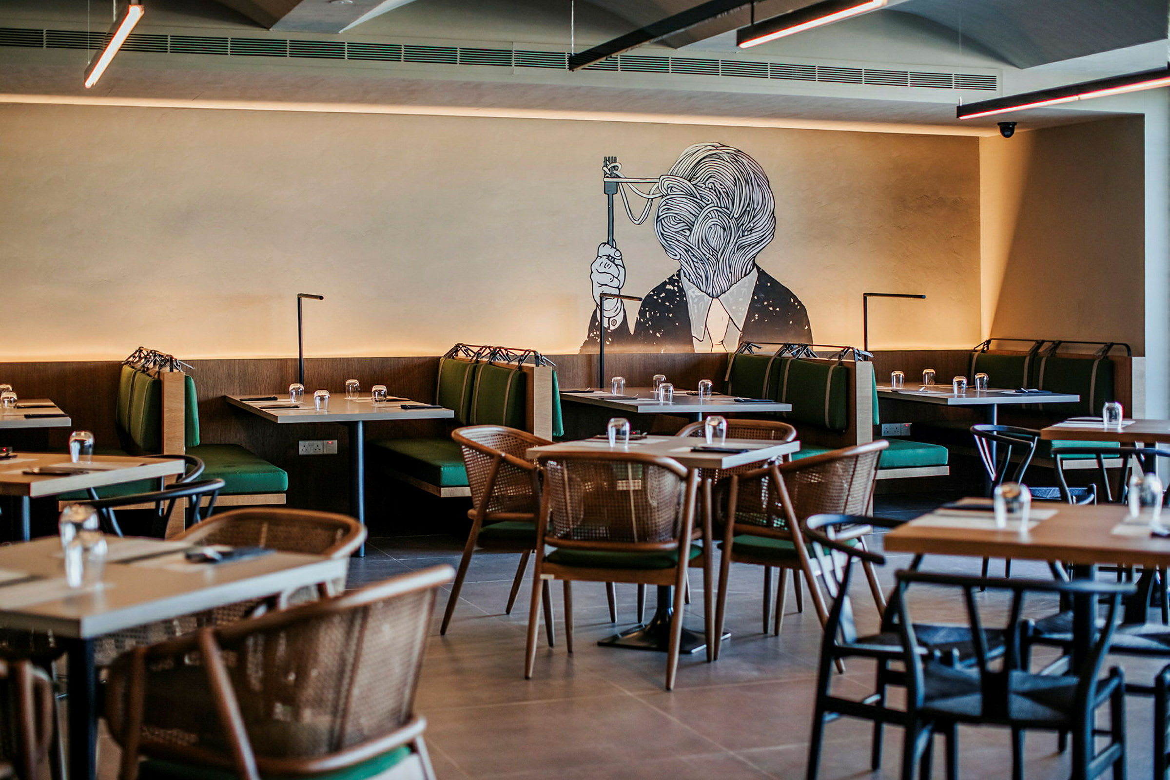 Ravintola, jossa on pöytiä ja vihreitä sohvia sekä seinämaalaus taideteoksesta. (Tekoälyn luoma teksti)