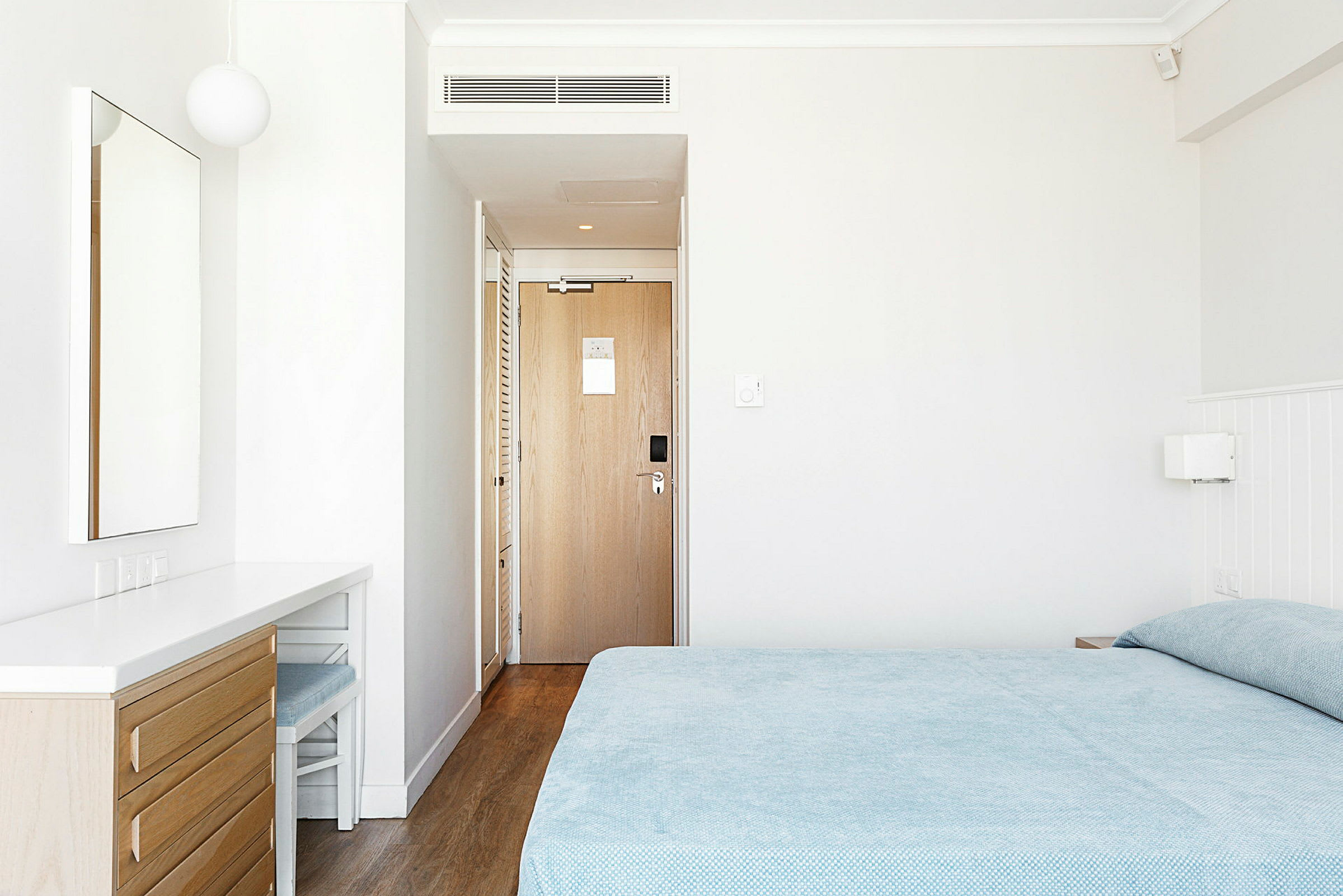 Hotellihuone, jossa sänky, peili lipaston päällä ja ovi. (Tekoälyn luoma teksti)